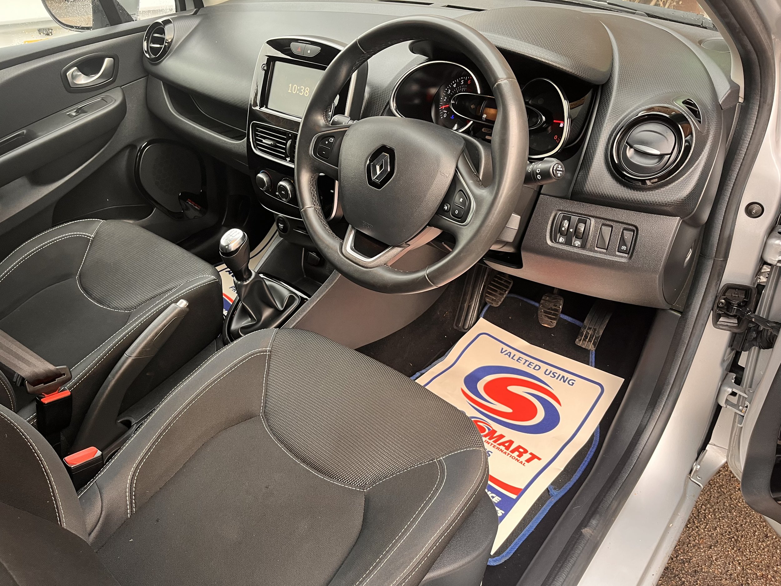 Interior view of a Renault car showing the steering wheel, dashboard, gear shift, front seats, and floor mats with a logo and text.