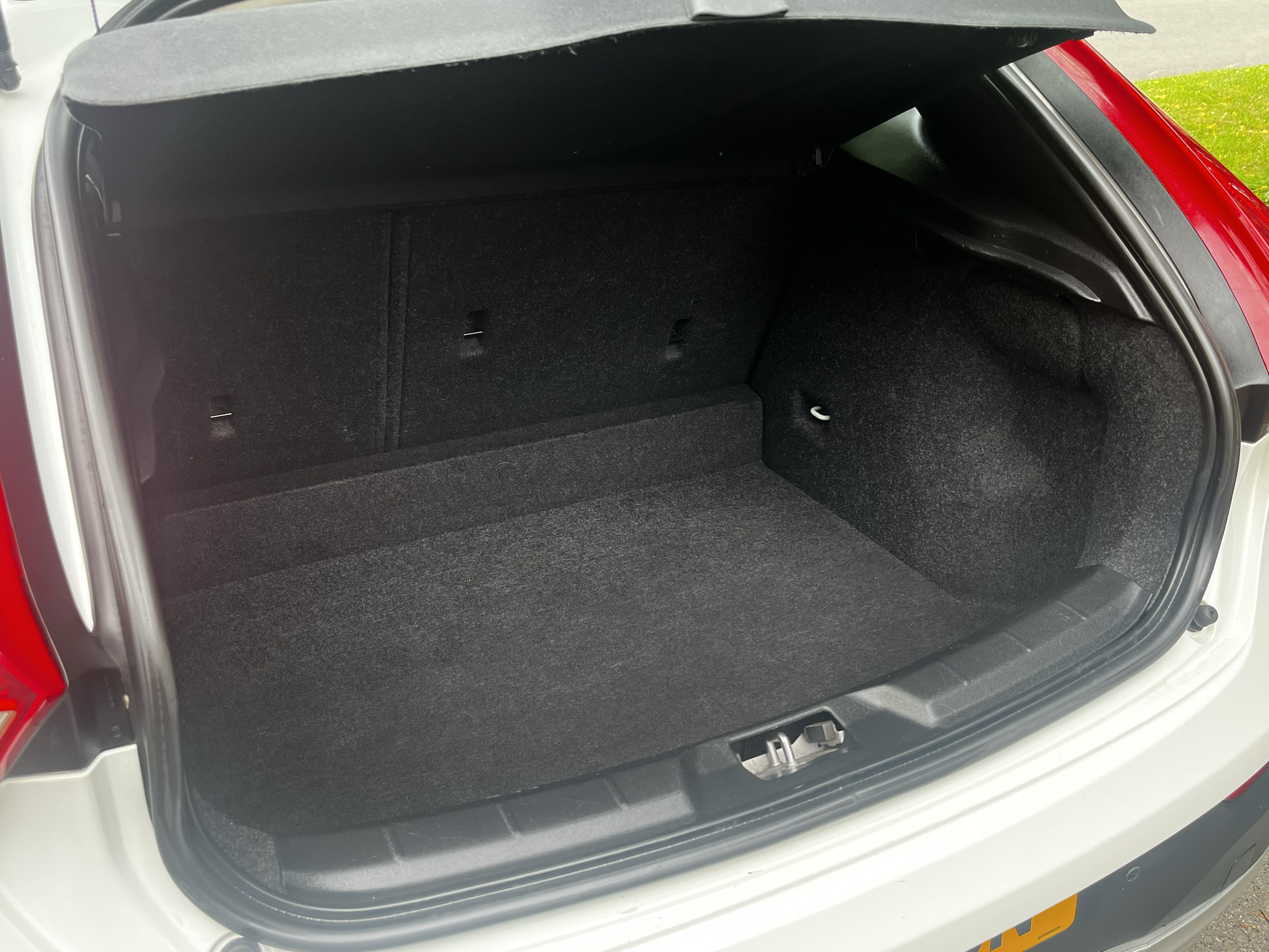 Open trunk of a white car, showing a spacious interior with black carpeted lining.