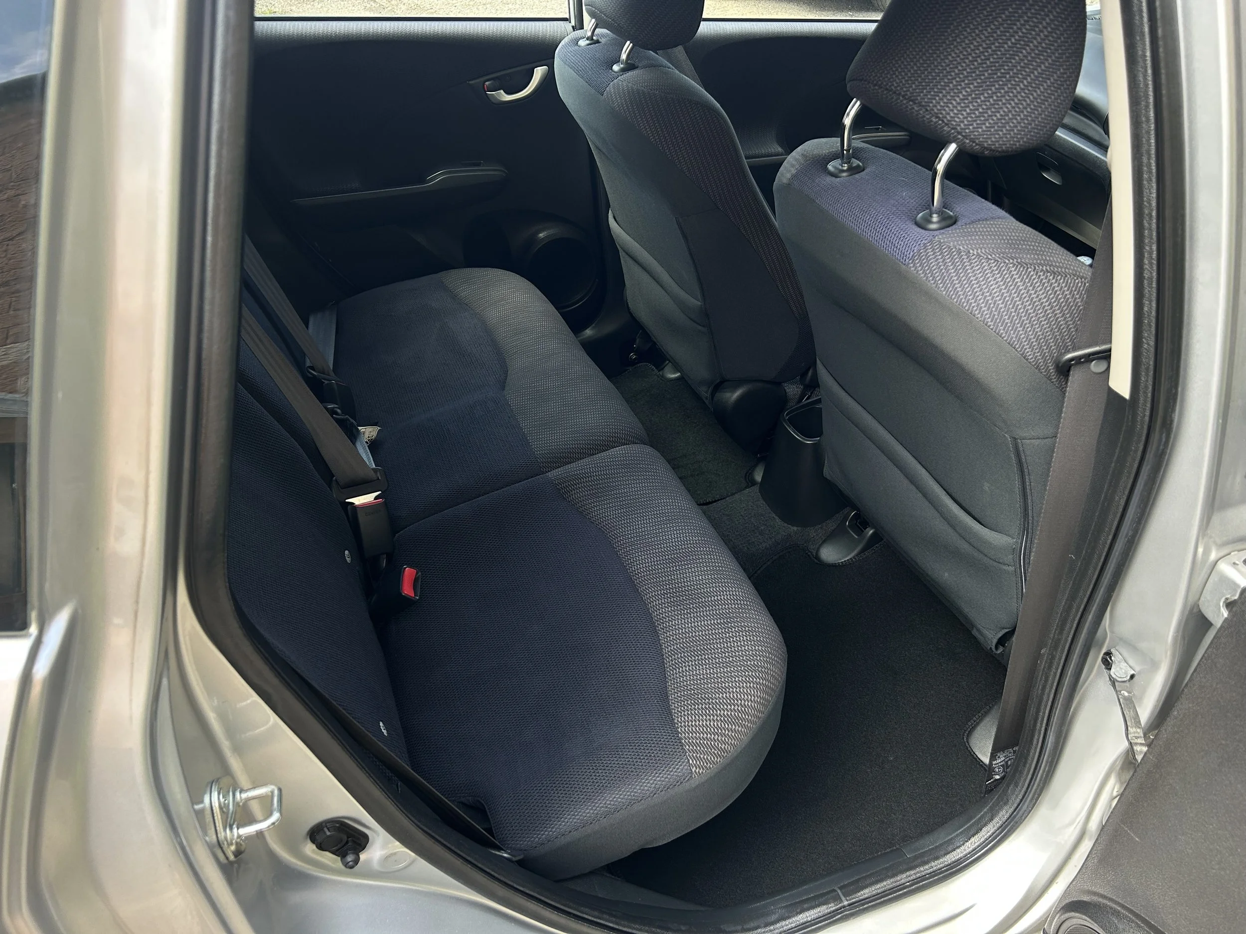 The interior of a car showing the back seat area with dark fabric upholstery, seat belts, and front seats with headrests.