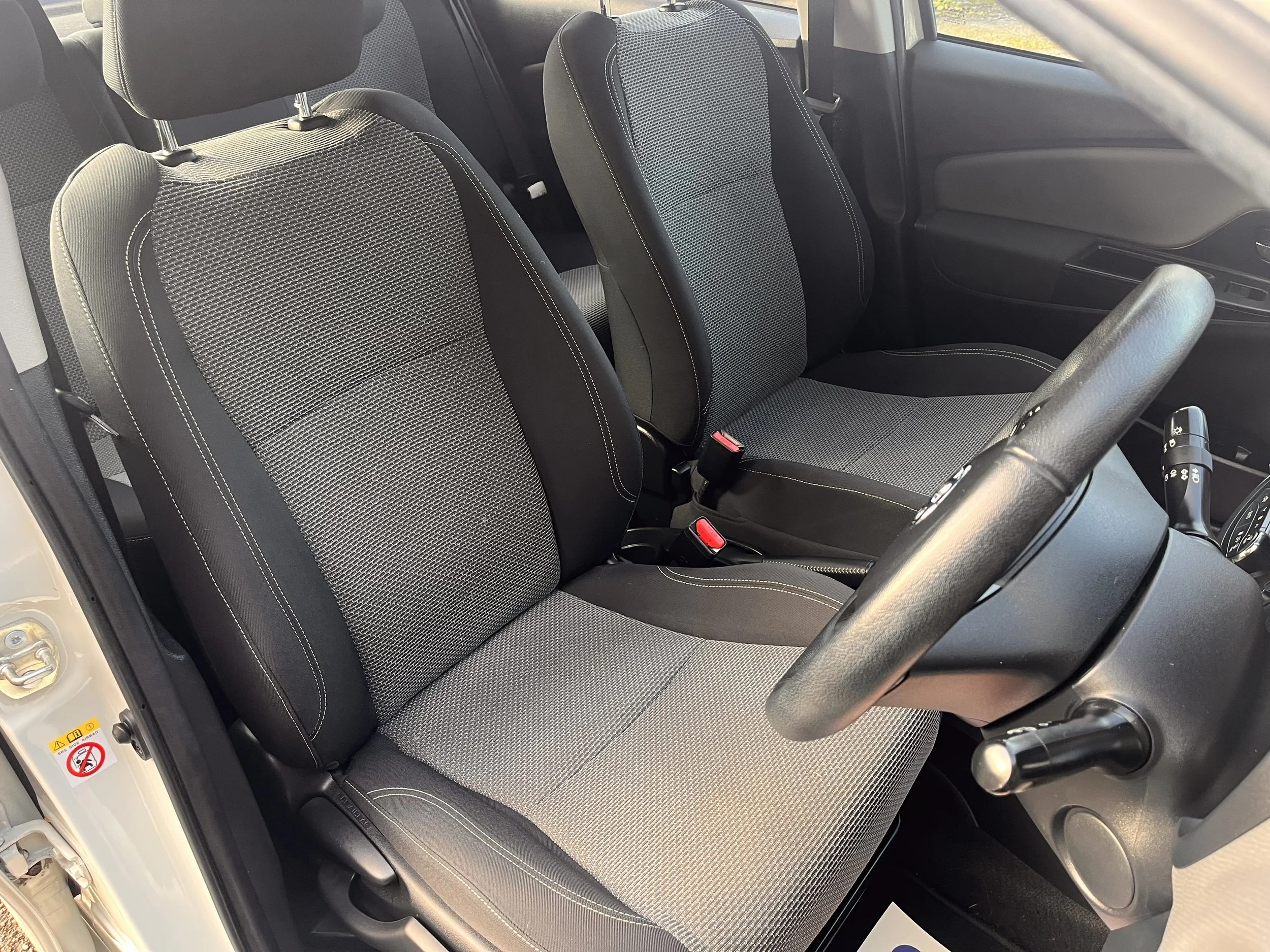 The interior of a car showing the front passenger and driver seats, both with black and gray fabric upholstery, a steering wheel, and part of the dashboard.