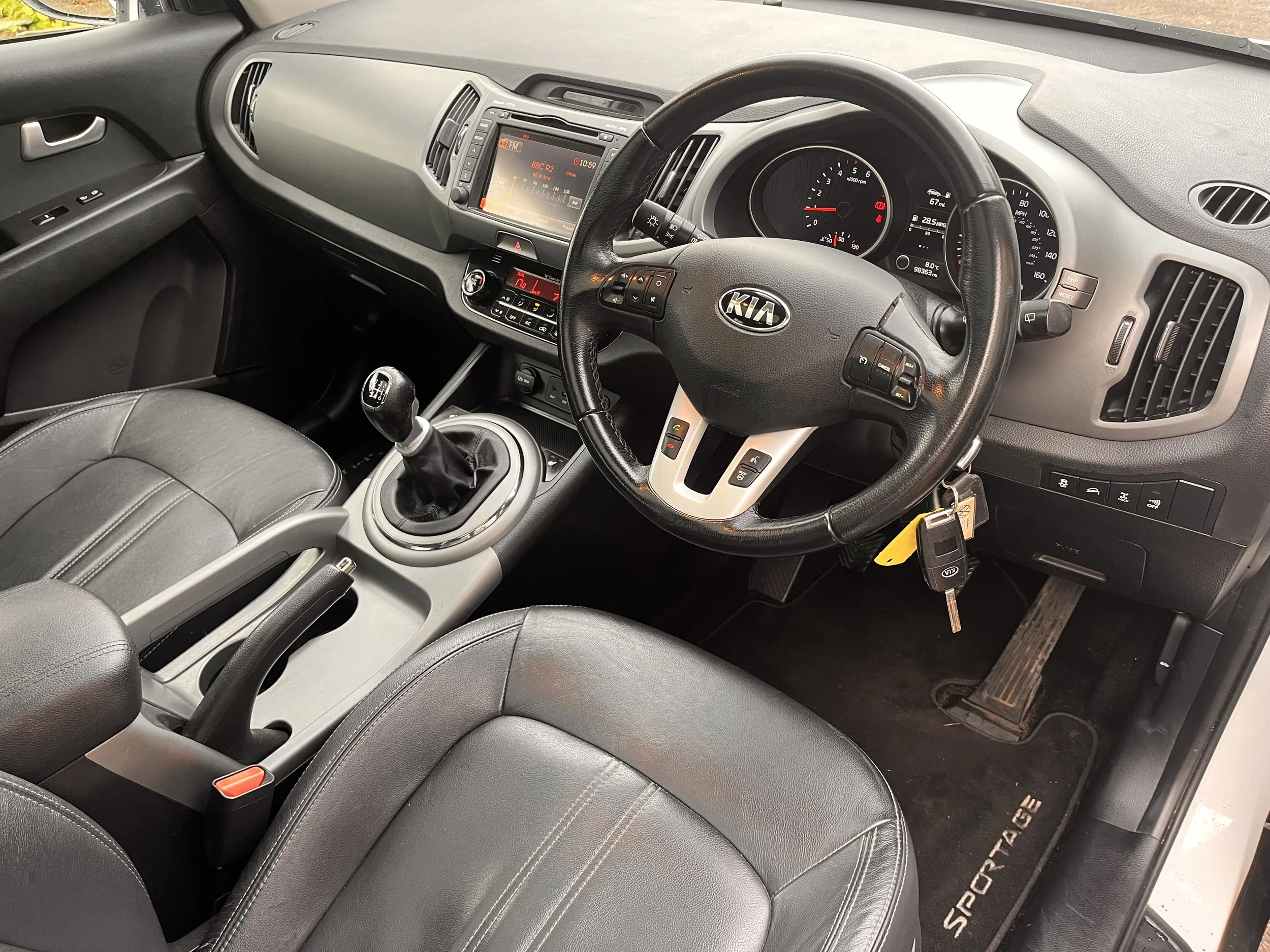 The interior of a Kia Sportage vehicle showing the driver's seat, steering wheel, dashboard, gear shift, and center console.