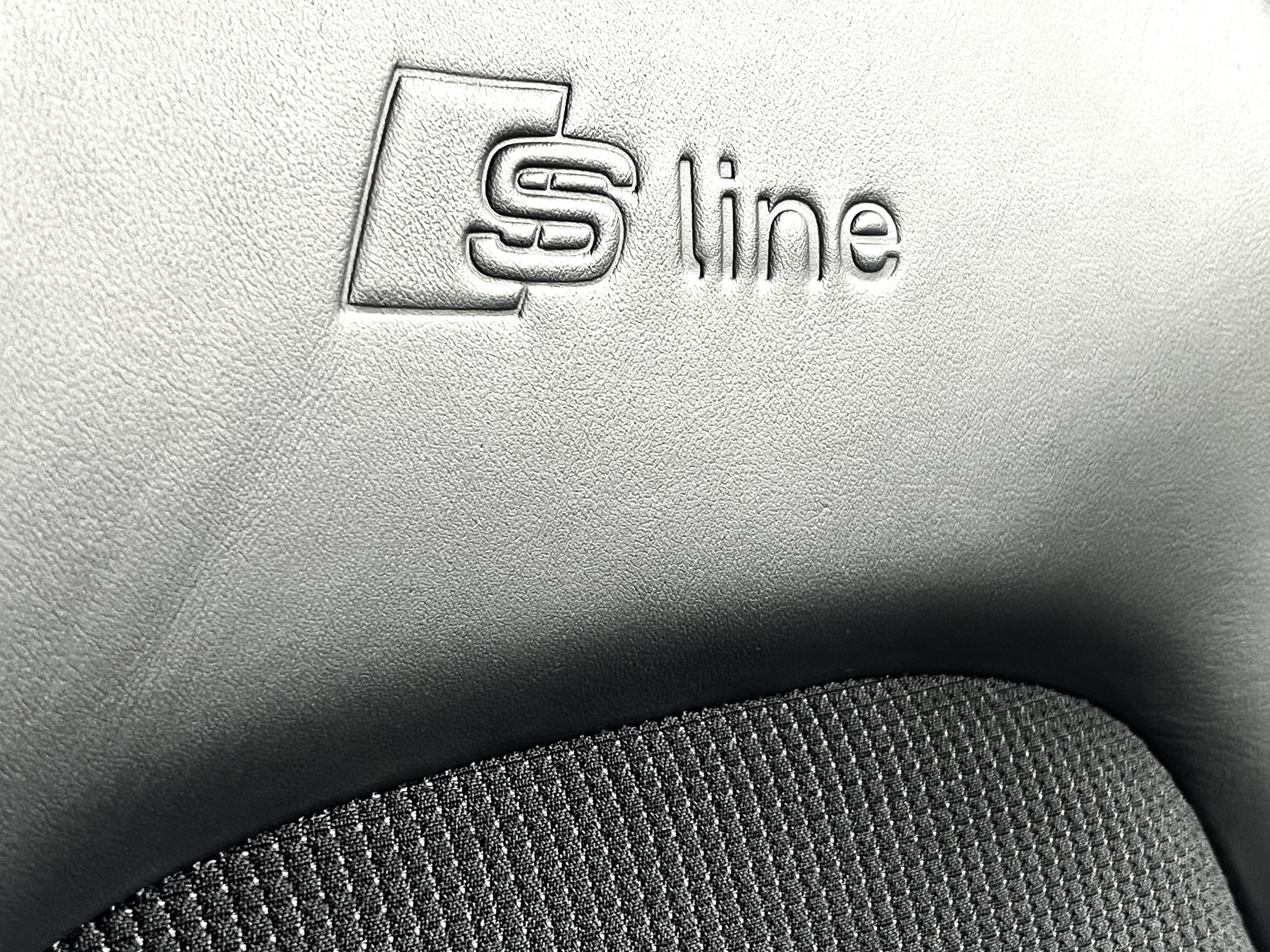 Close-up of a textured gray car dashboard with an embossed 'S line' logo.