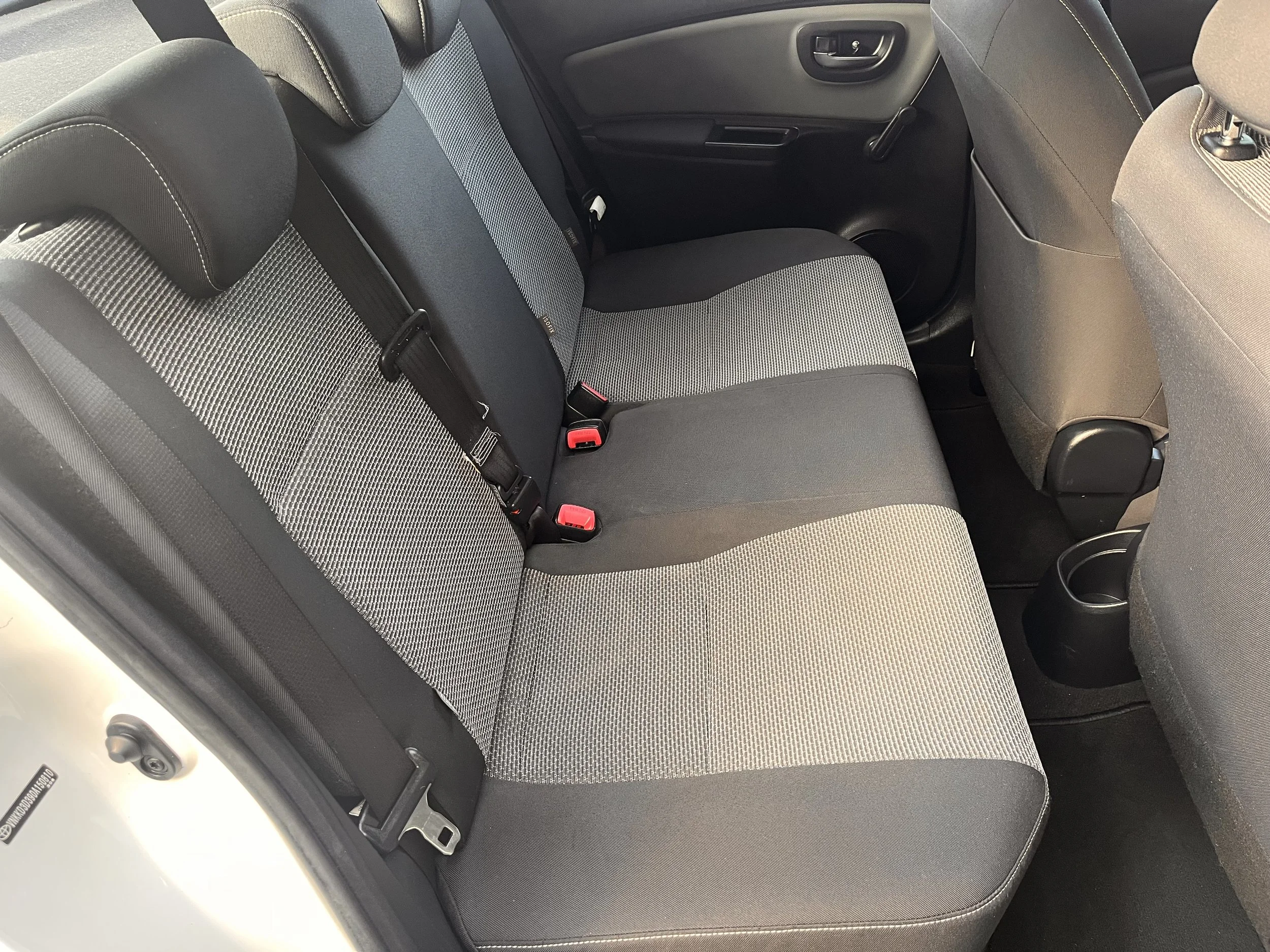 The backseat interior of a car with a gray and black patterned fabric seat and black door panel.