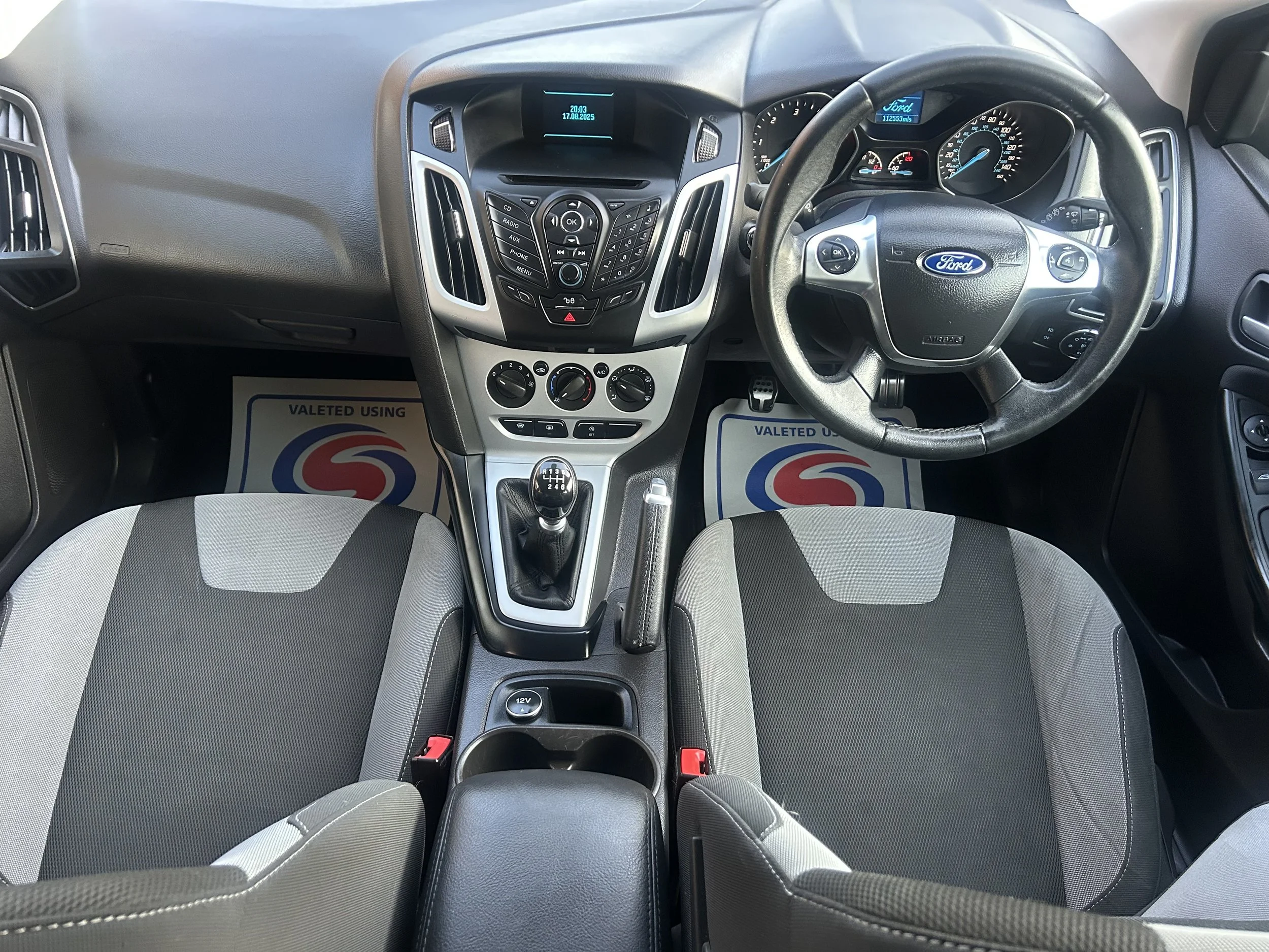 Interior view of a Ford car dashboard with steering wheel, gear shift, and front seats.