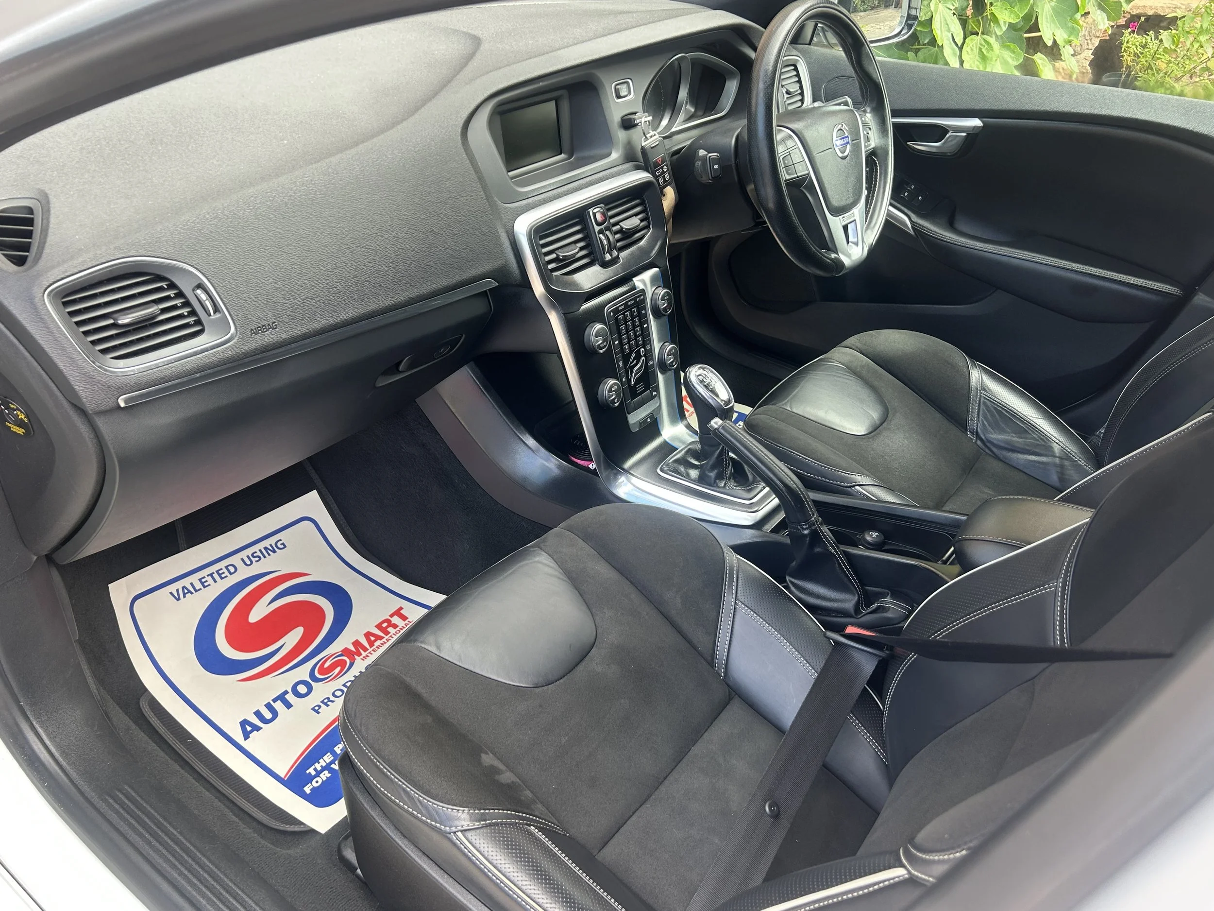 Interior of a car showing driver and passenger seats, dashboard with controls, gear shift, and steering wheel, with a floor mat labeled Auto Smart.