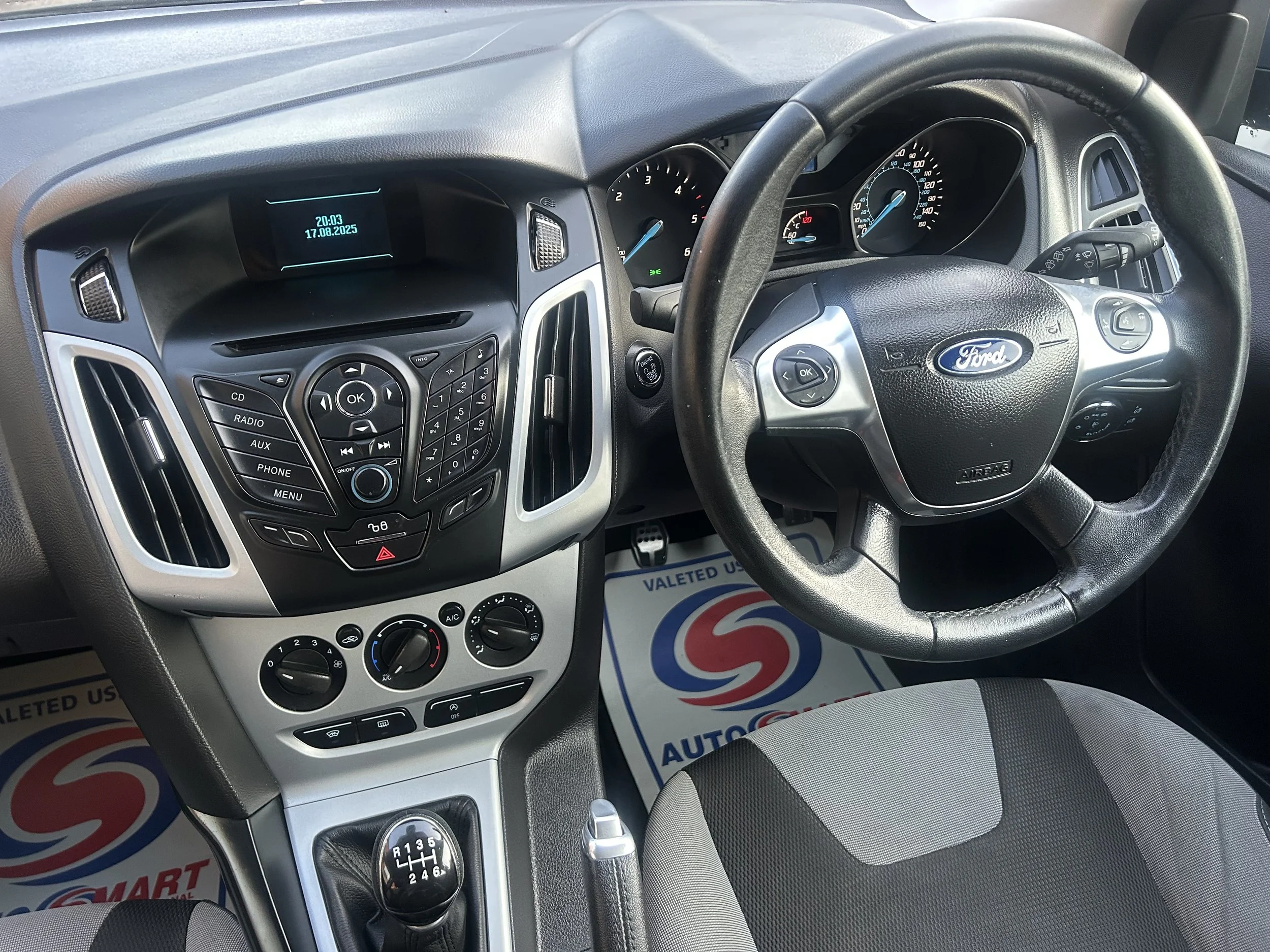 Interior of a Ford vehicle showing the steering wheel, dashboard, center console with controls, gear shift, and driver's seat.