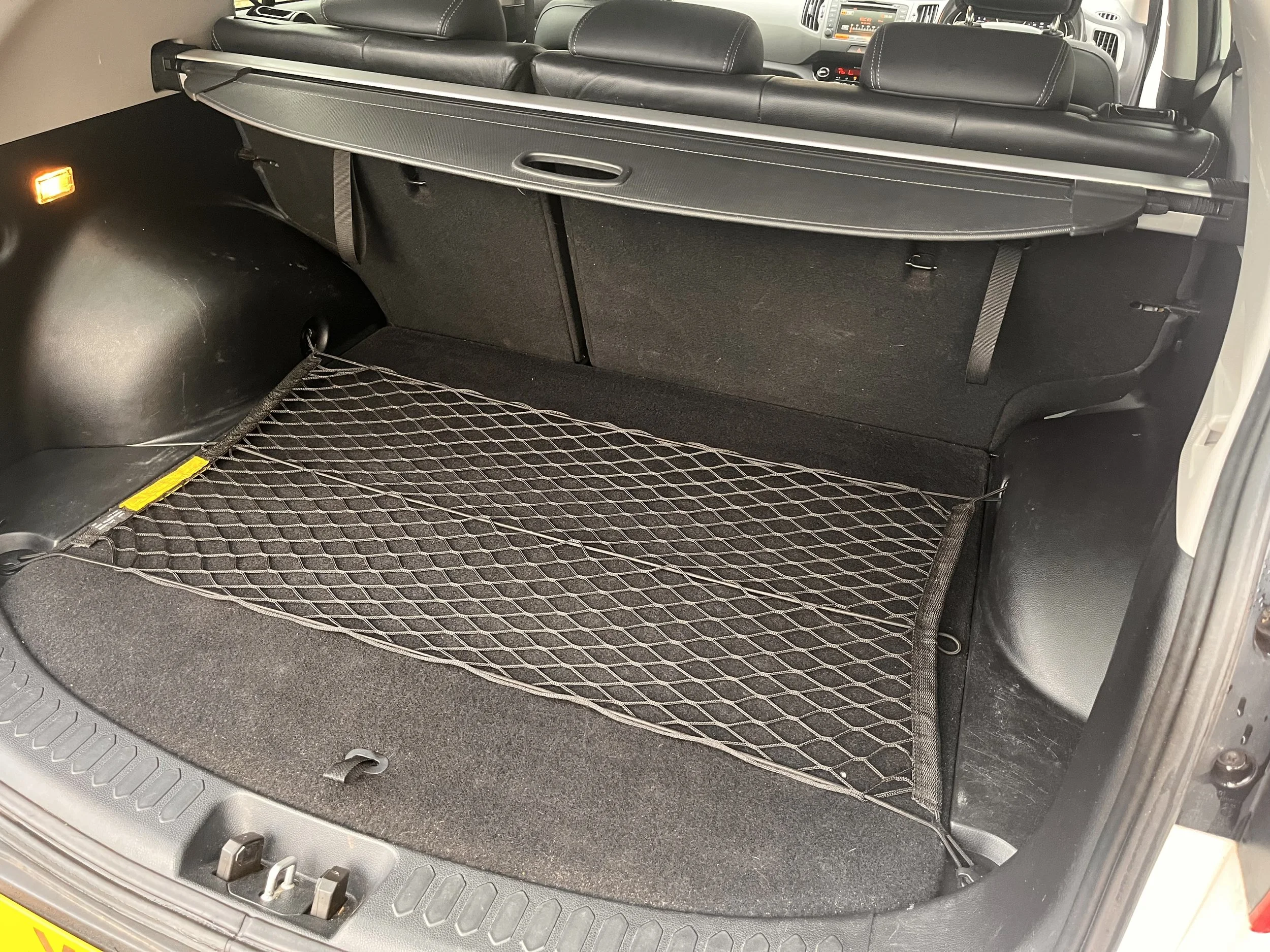 The open trunk of a car showing a cargo net on the floor, with a black interior and rear seats visible.