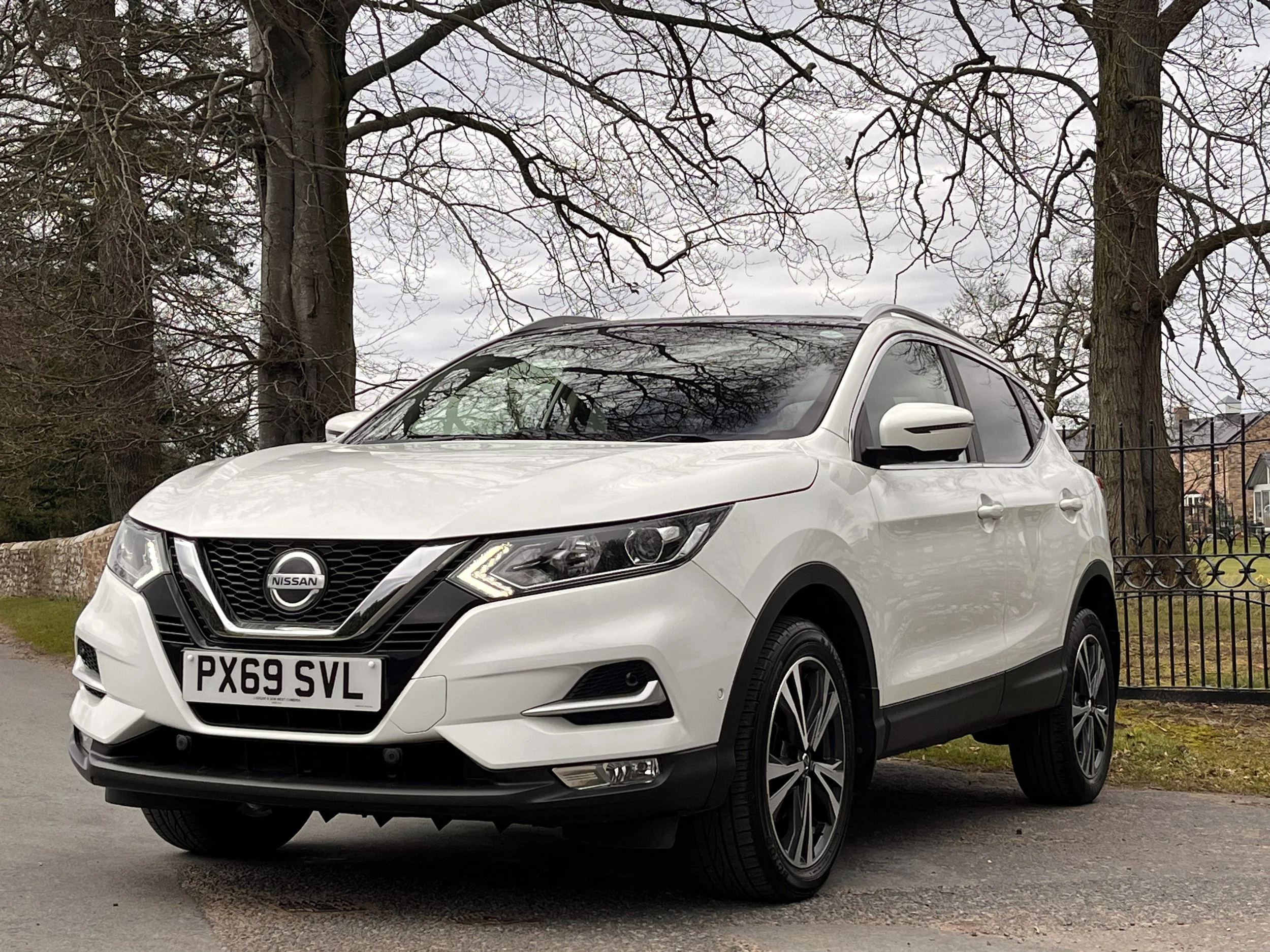 White Nissan SUV parked on a street with trees and houses in the background.