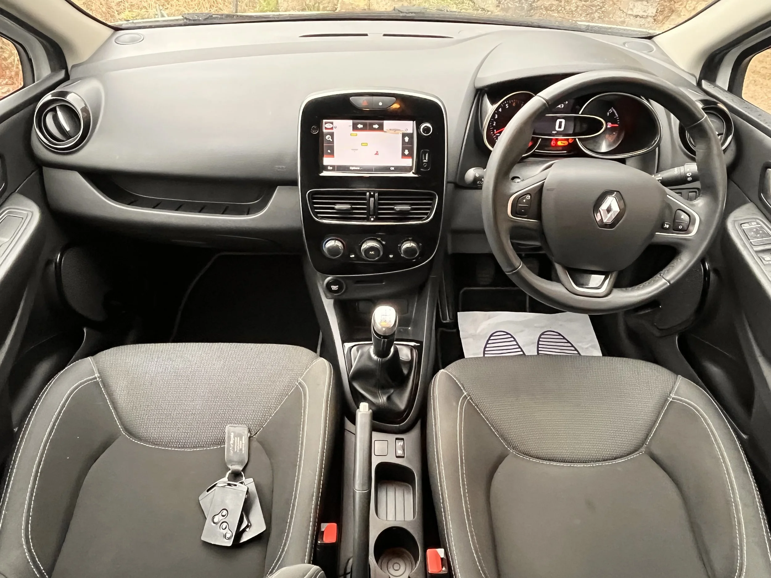 Interior of a modern Renault car showing the dashboard, steering wheel, gear shift, and two front seats with key fob on the left seat.
