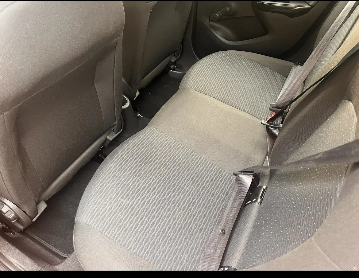 Backseat of a car showing fabric upholstered seats and seat belts.