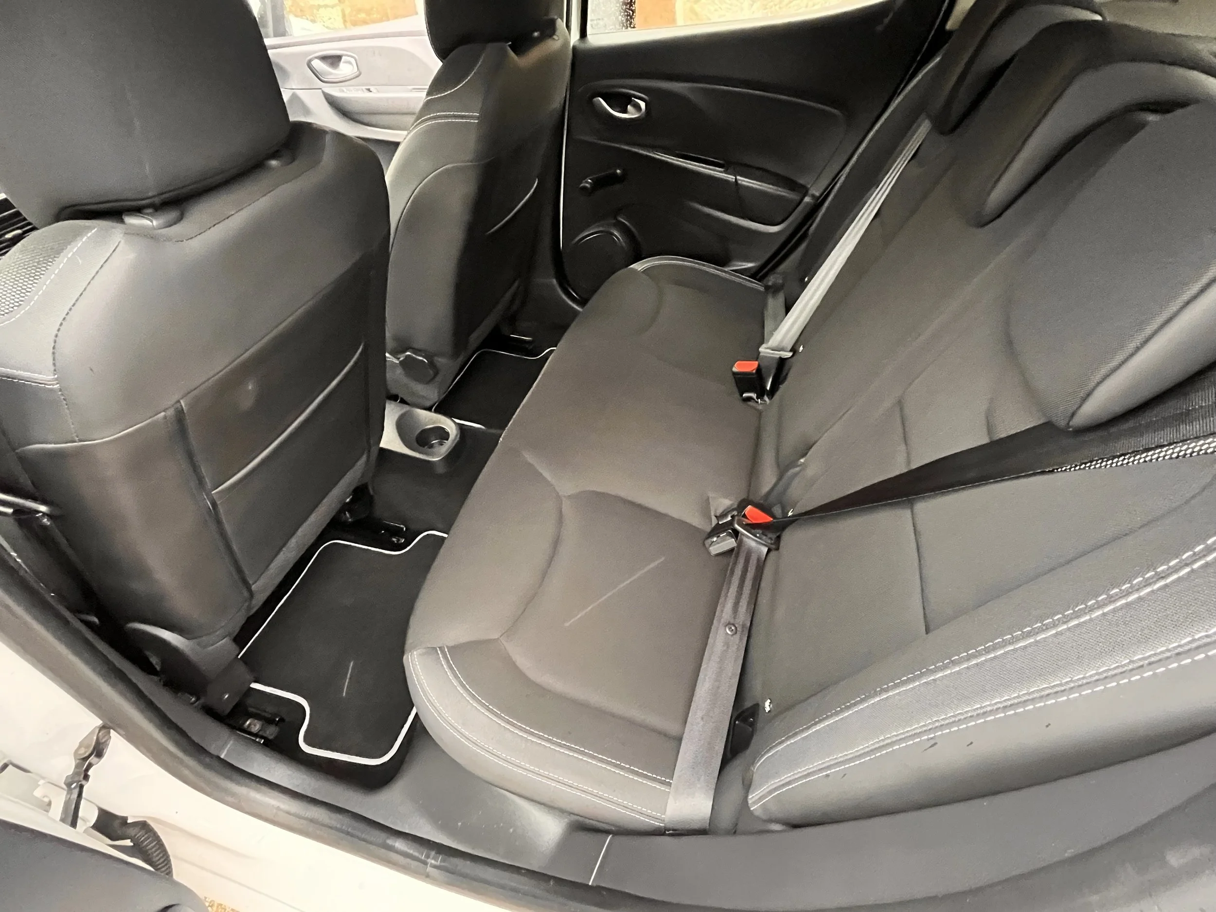 Interior of a car showing the back seat with black seats and seat belts, and the back of the front seats with storage pockets.