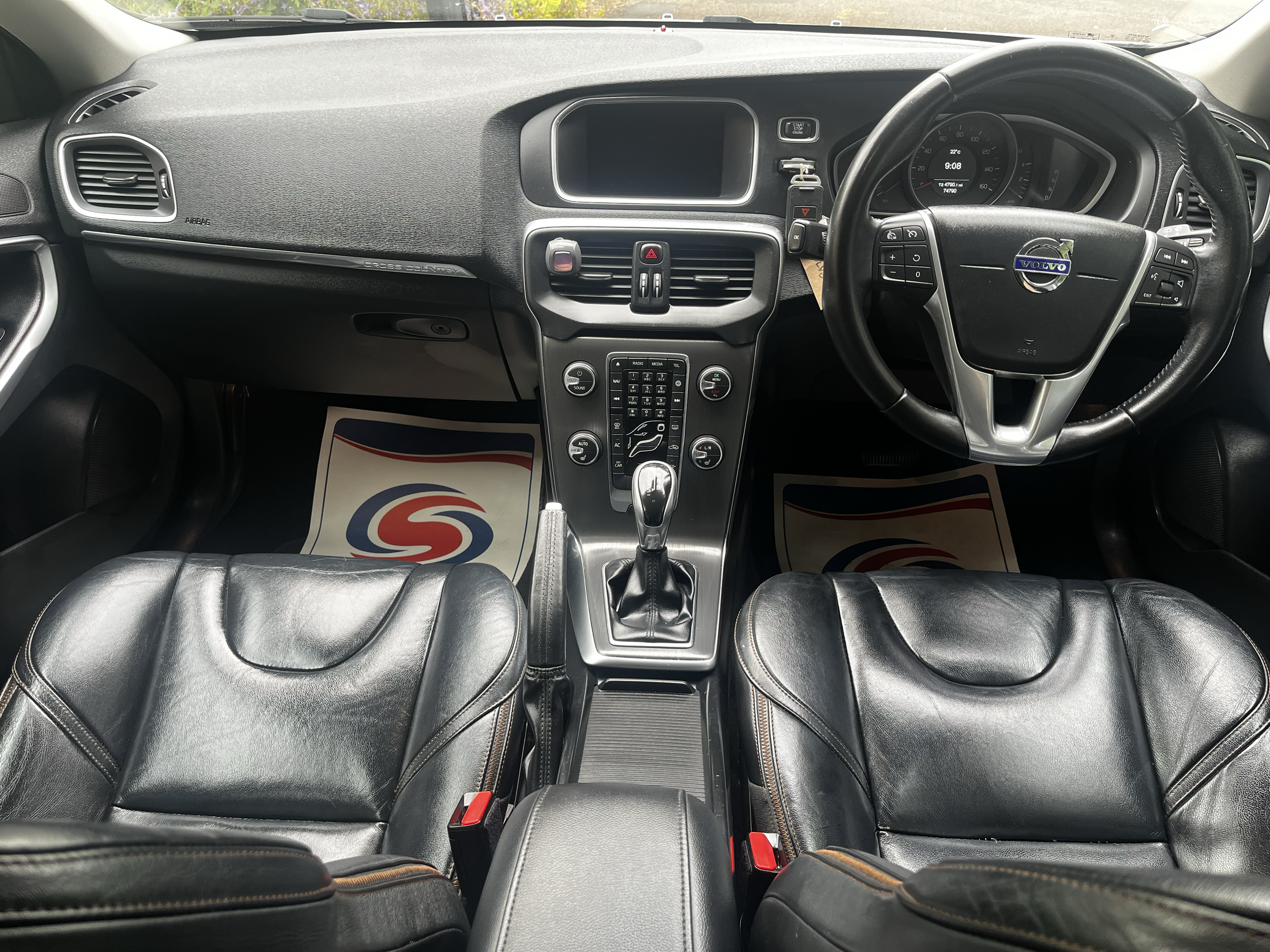 The interior of a Volvo car, showing the dashboard, steering wheel with Volvo logo, and leather seats.
