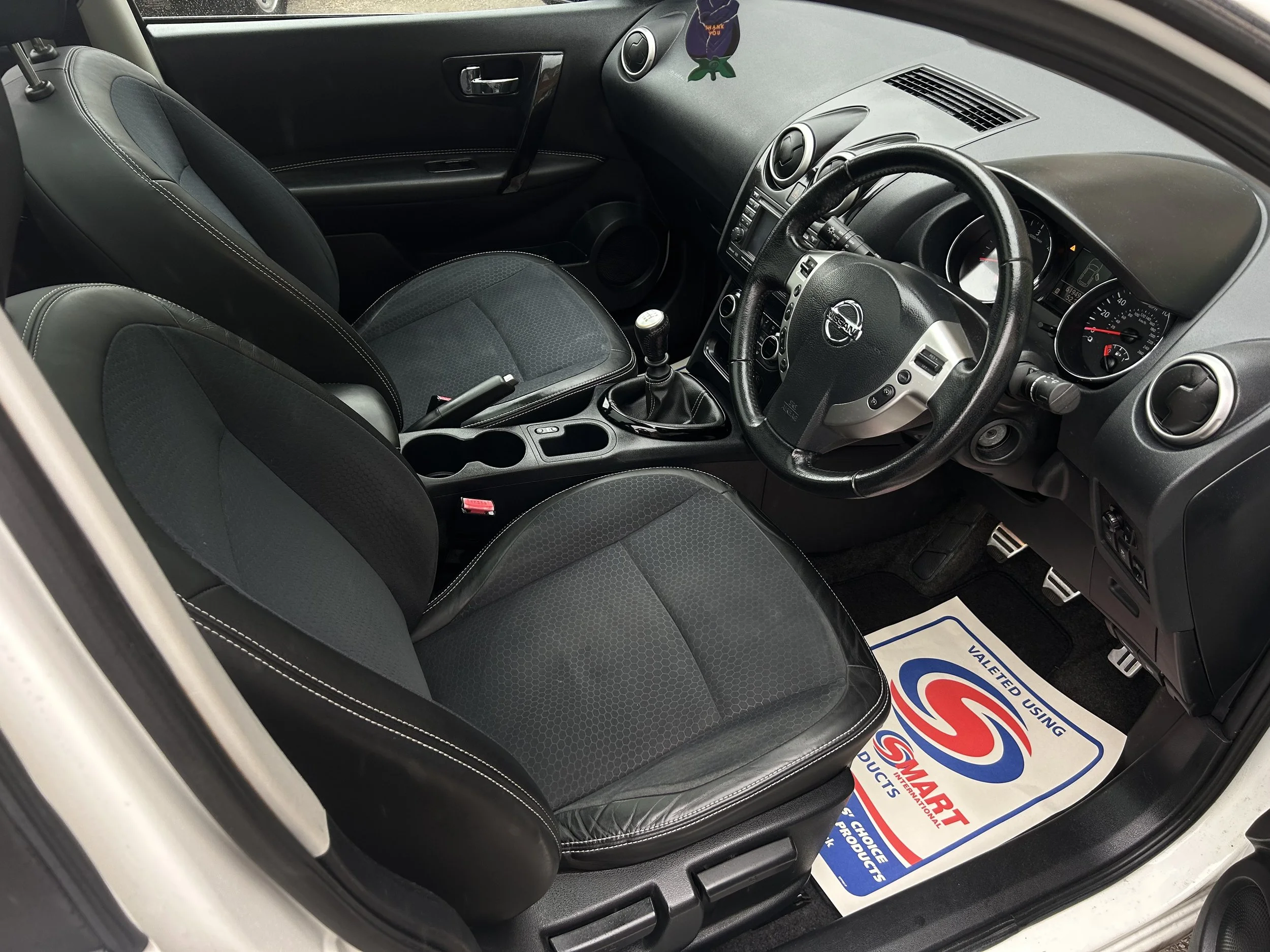 Interior of a Nissan car showing the front seats, steering wheel, dashboard, and floor mat.