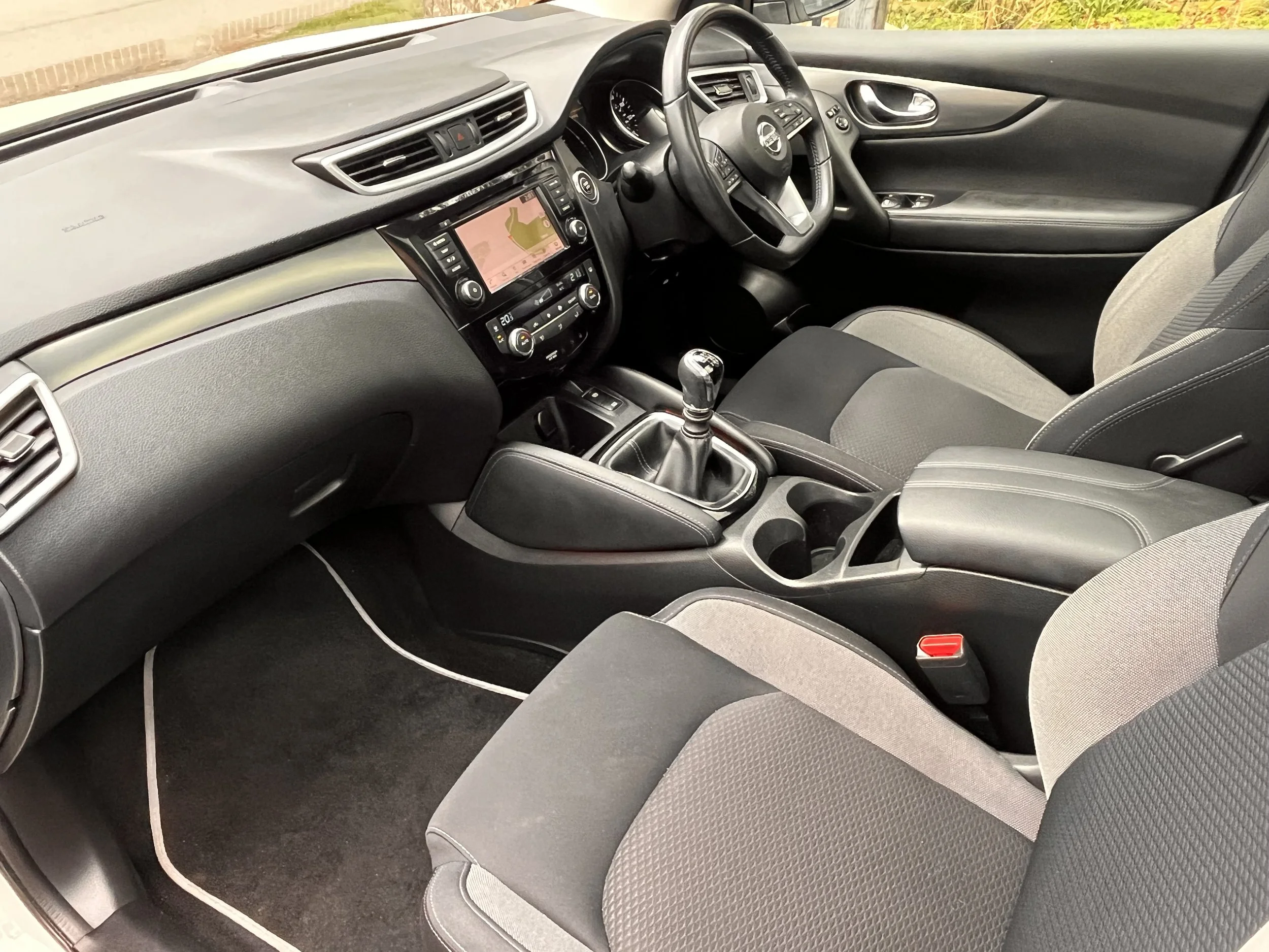 Interior of a Nissan vehicle showing the dashboard, steering wheel, gear shift, and front seats.