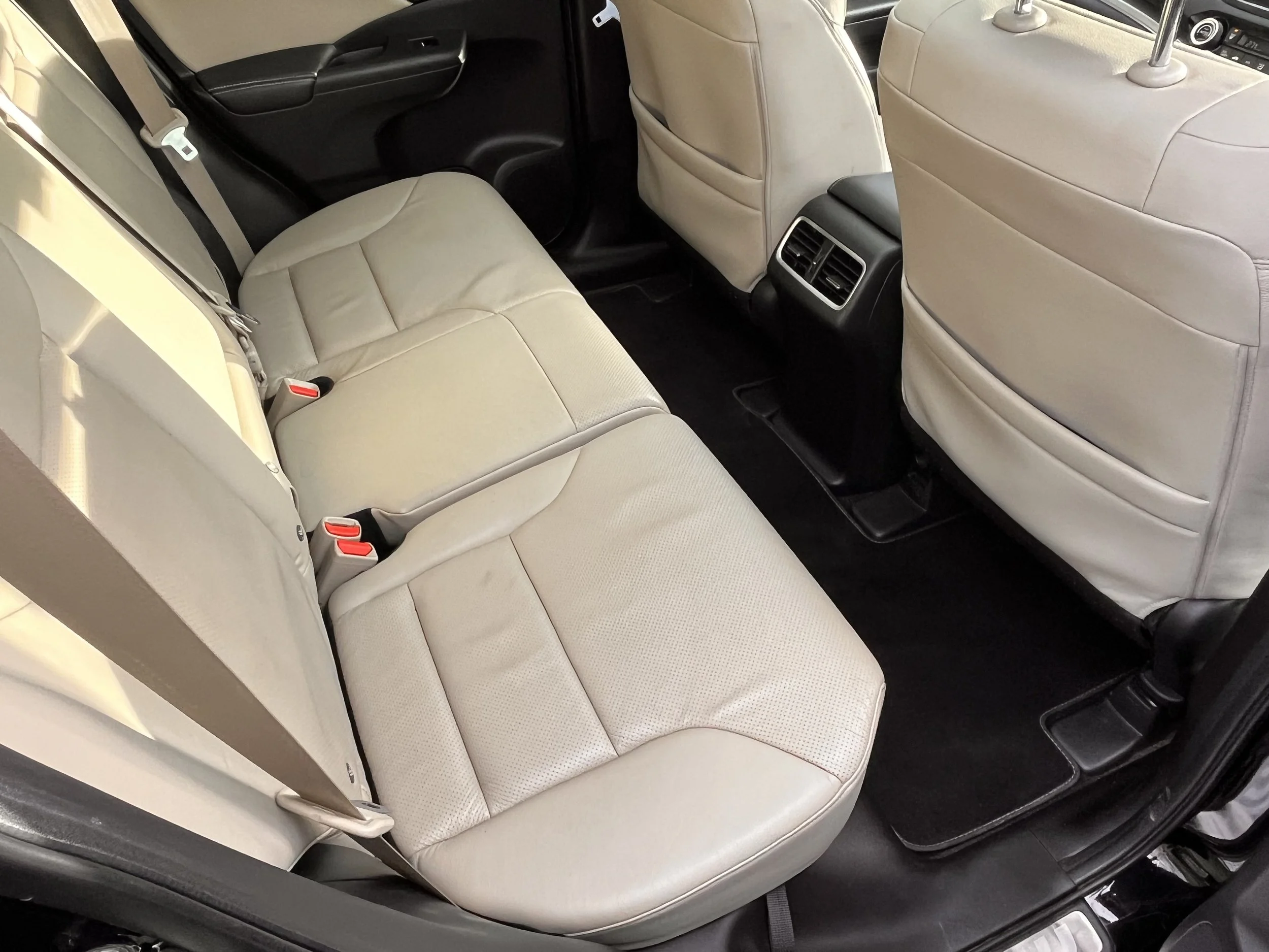 The interior of a car showing beige leather back seats, black floor mats, and the back of beige front seats.