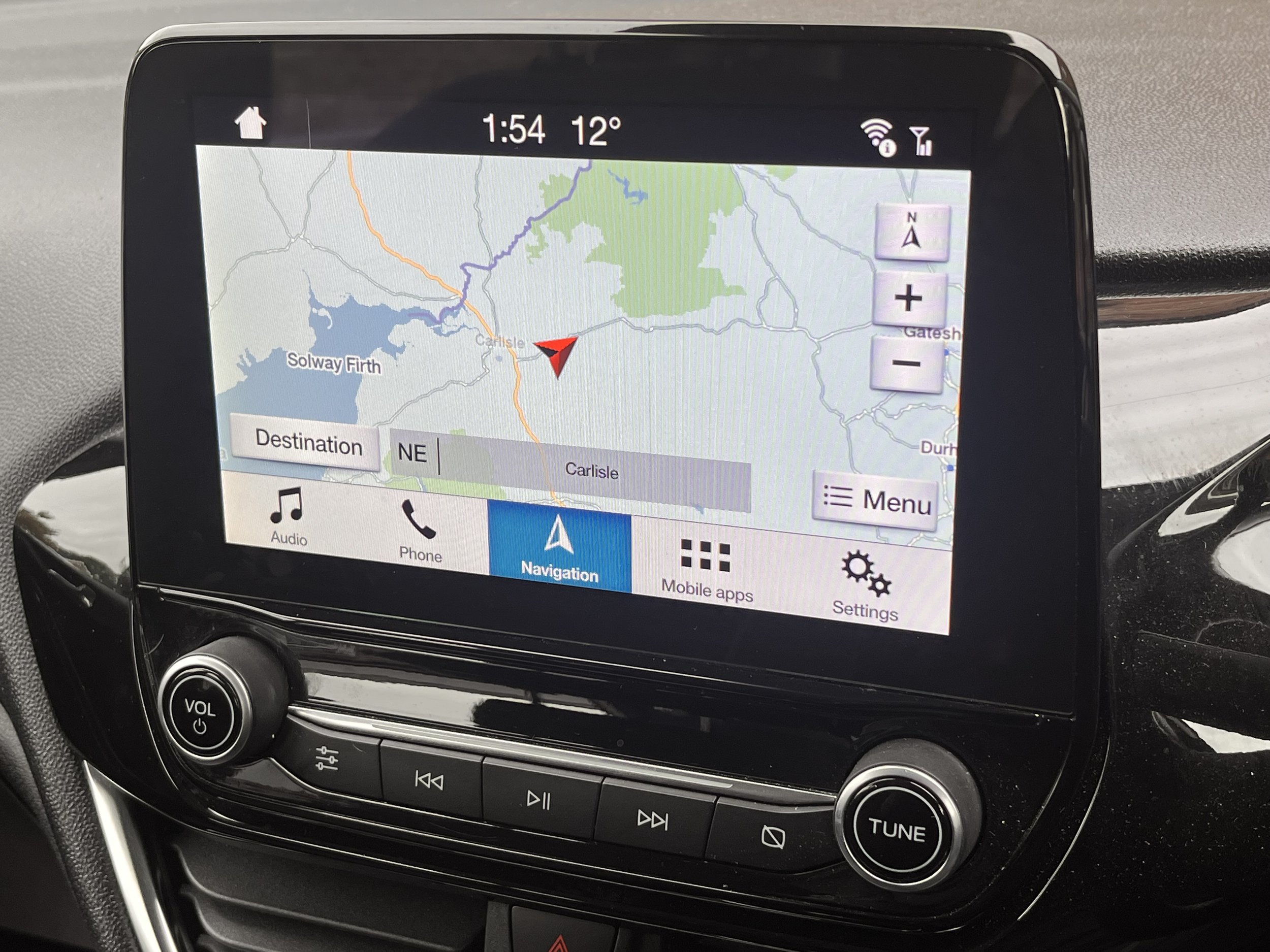 Car infotainment screen showing a navigation map focused on Carlisle, with options for audio, phone, navigation, mobile apps, and settings at the bottom.