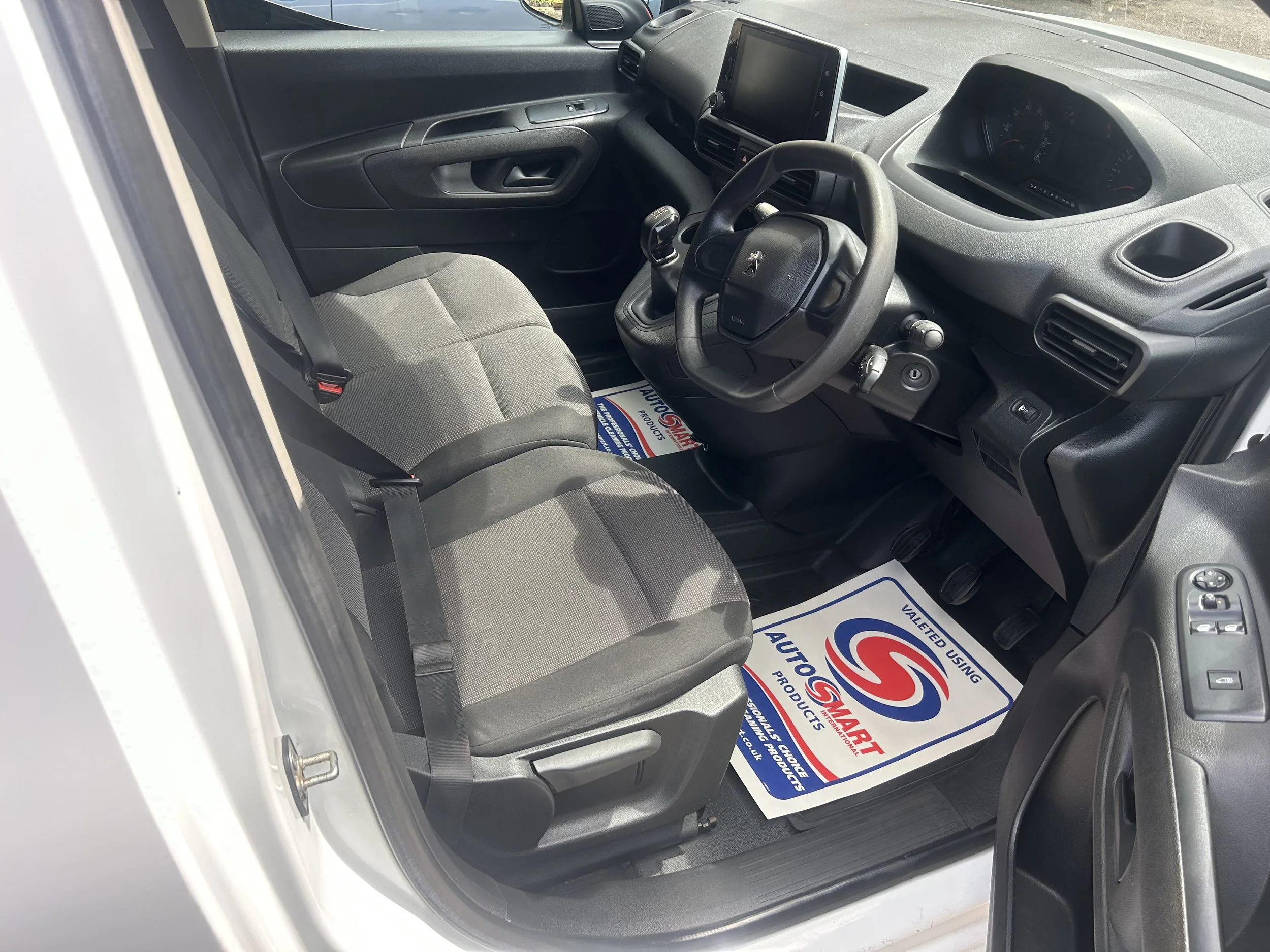Interior of a vehicle showing the driver's seat, steering wheel, dashboard, and a passenger seat with floor protection mats.