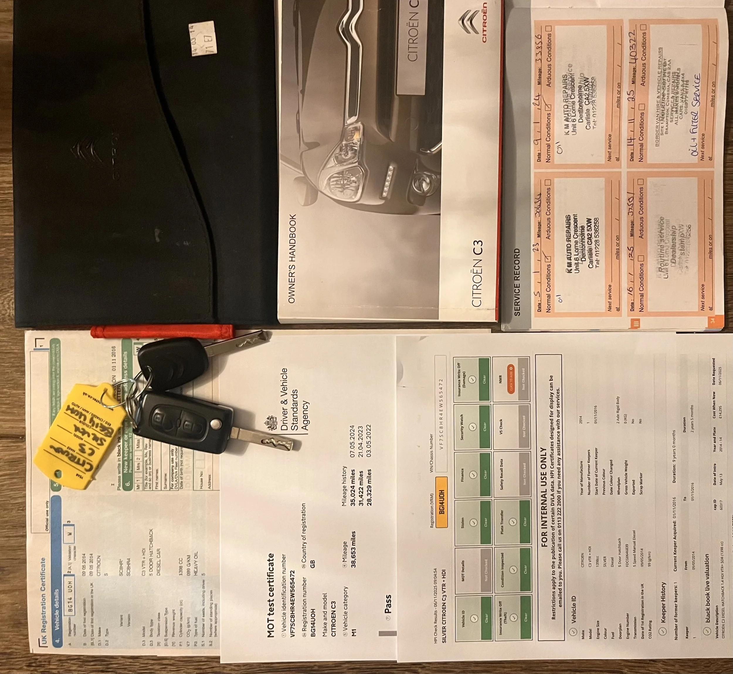 Car keys on a car registration document, owner's manual for a Citroën C3, and vehicle service record book with maintenance stamps.