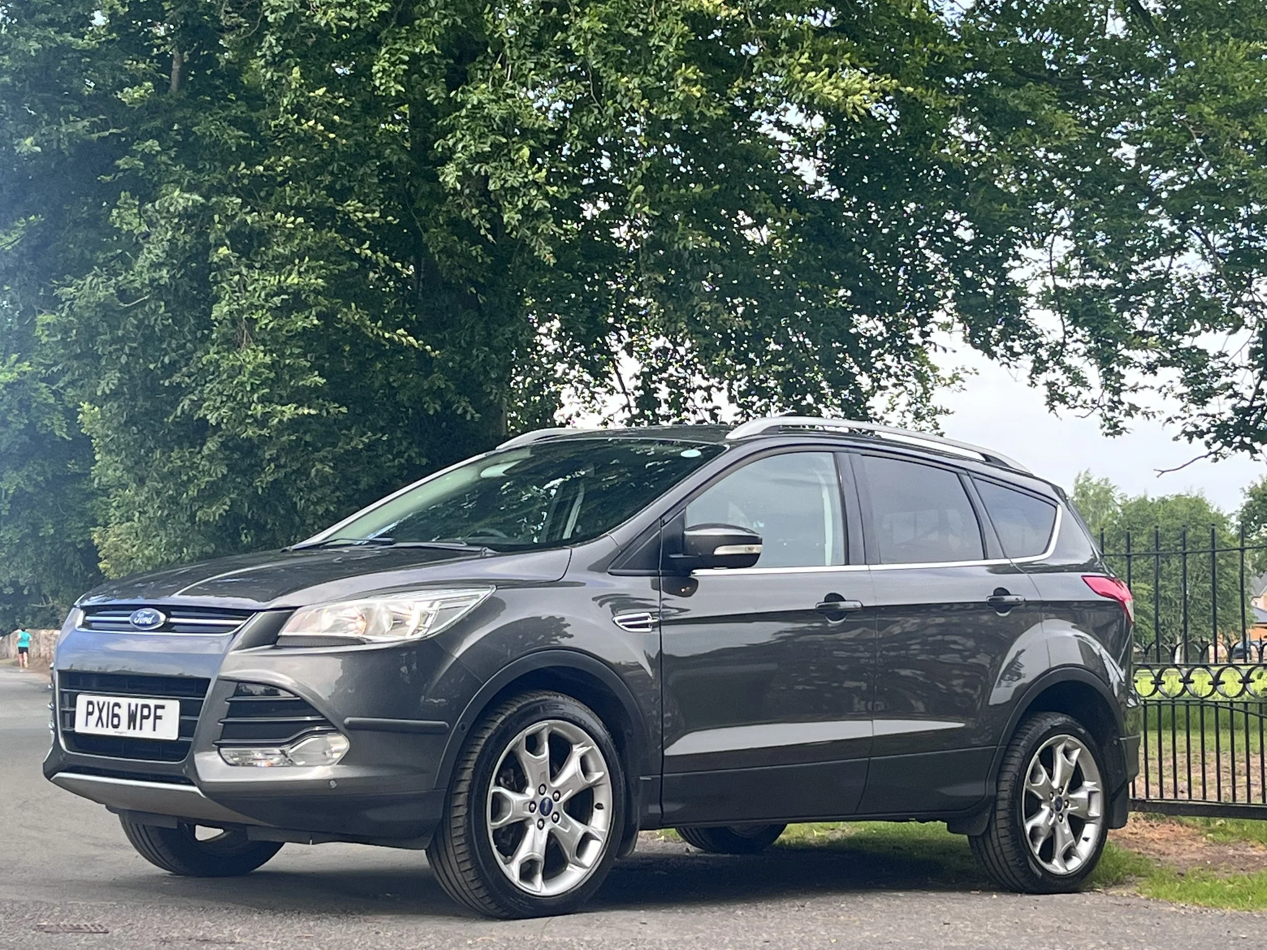 A black Ford SUV parked on a street with trees and a fence in the background.