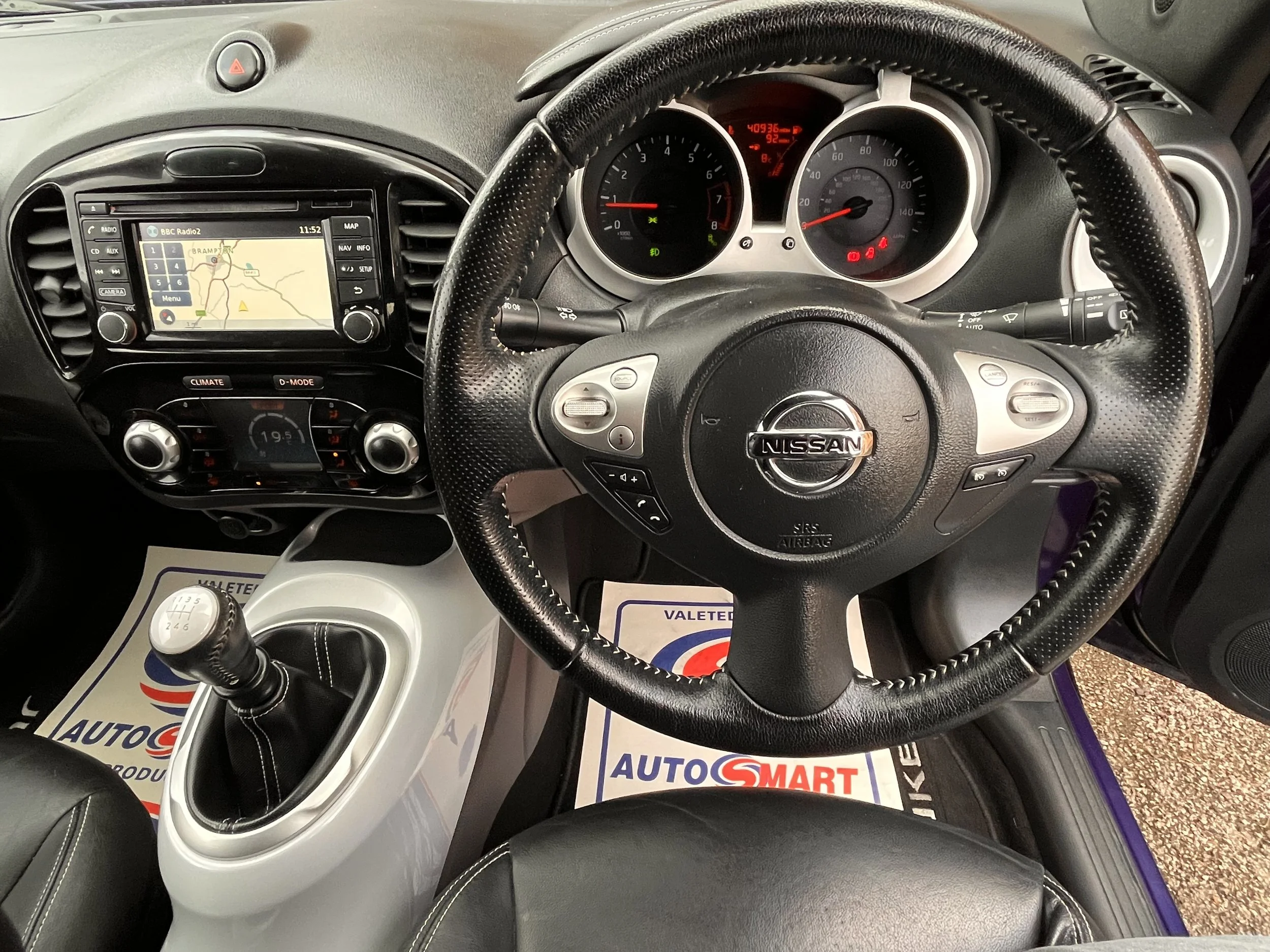 Interior of a Nissan vehicle showing the steering wheel, dashboard, touchscreen display, and gear shift lever.
