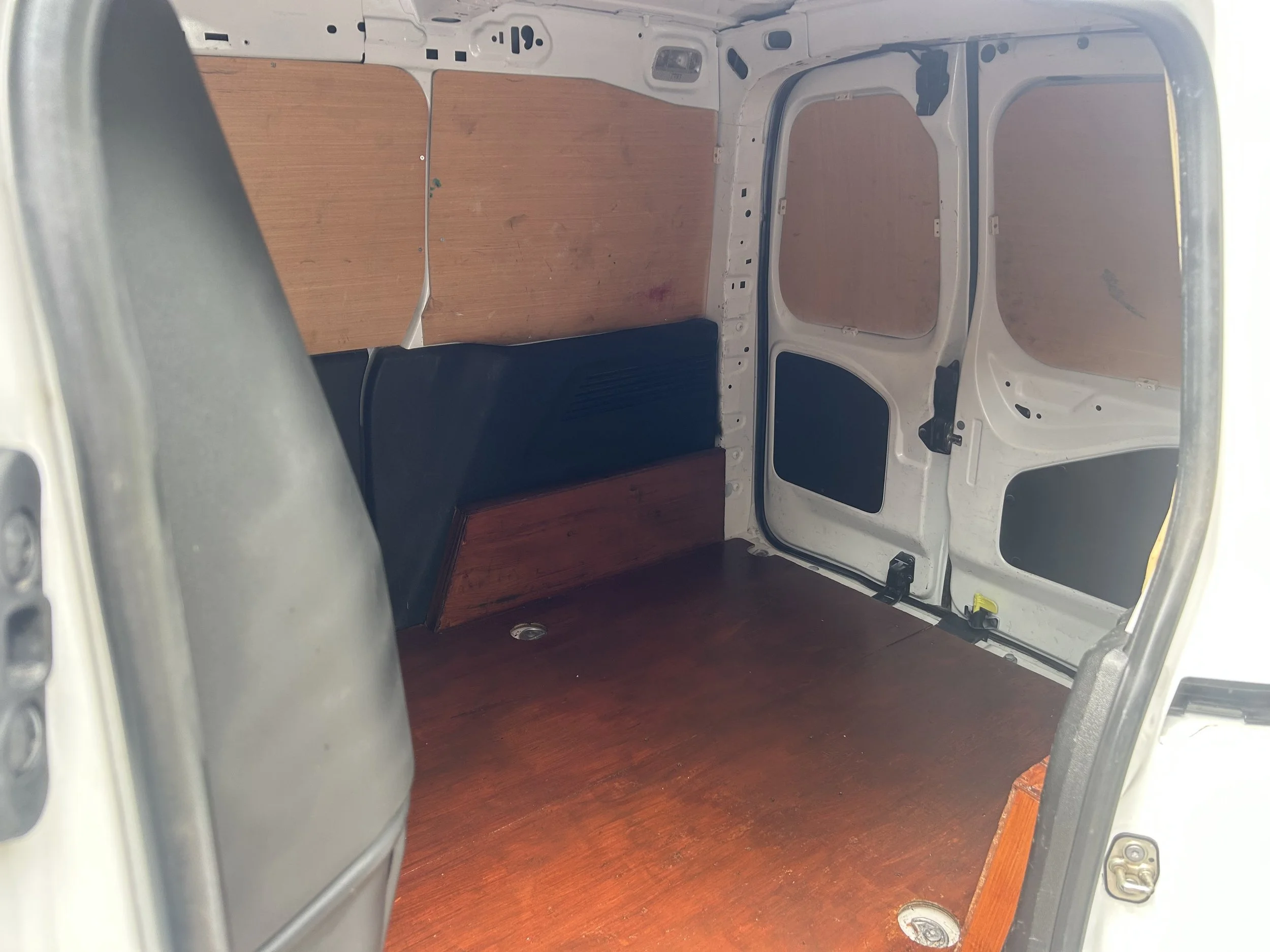 Empty cargo space of a van with wooden paneling on the walls and floor, and black seats folded against the side.