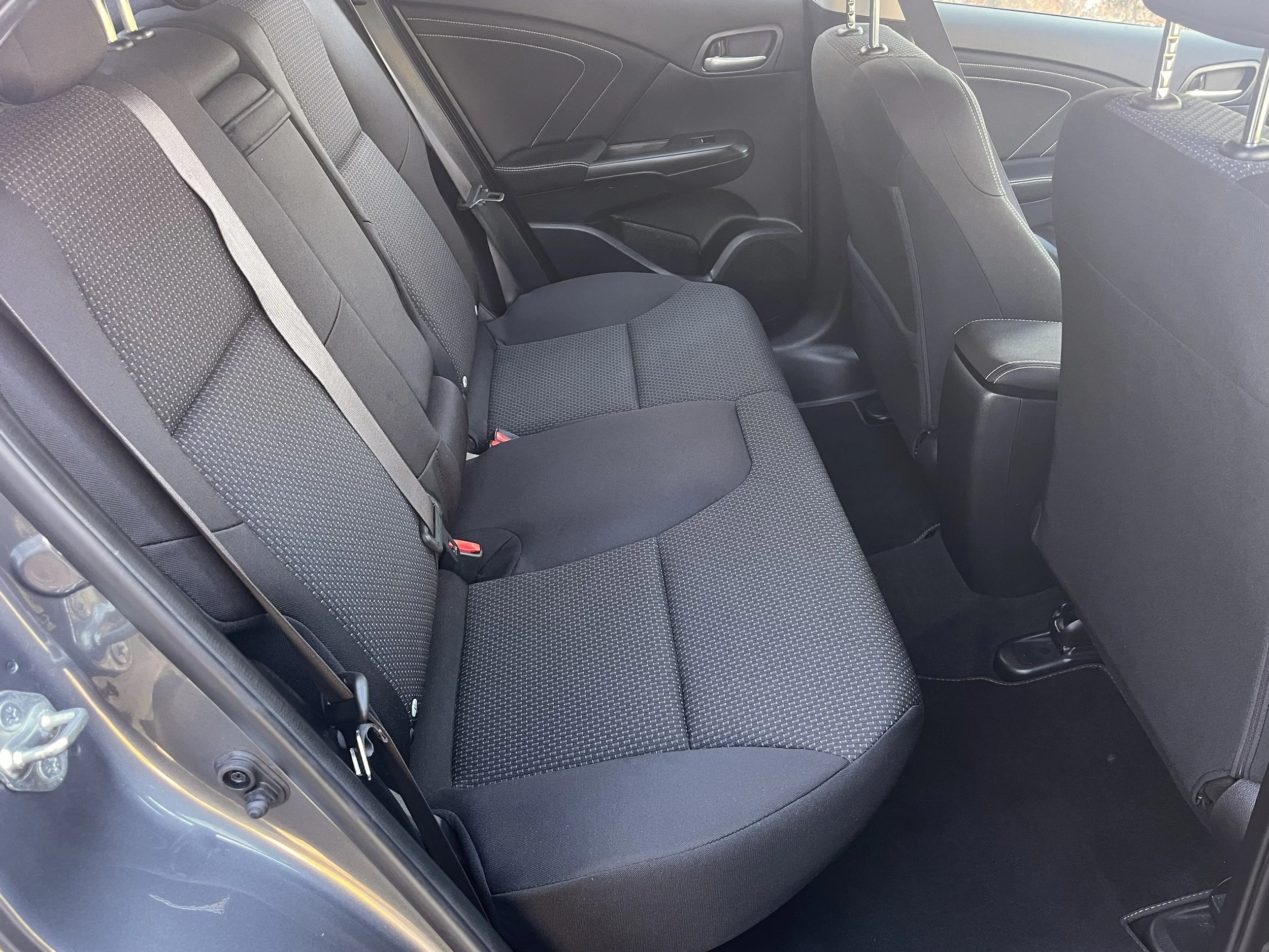 Interior of a car showing the back seat area with three black cloth seats and seat belts.