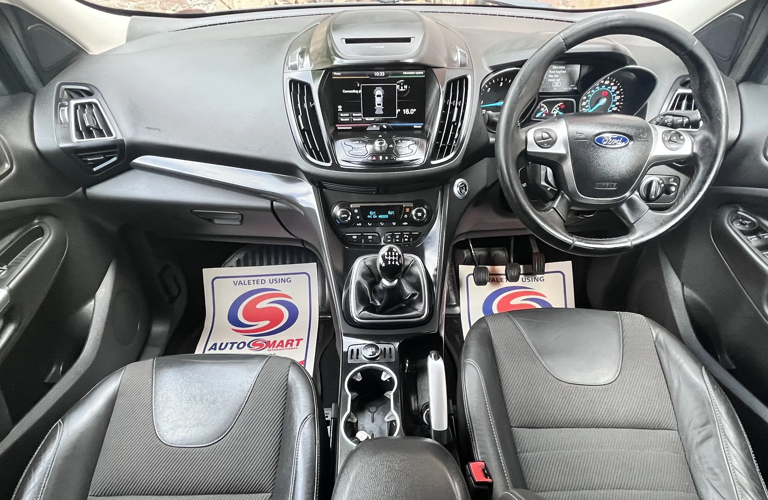 Interior of a Ford vehicle showing the steering wheel, dashboard, gear shift, and front seats with AutoSmart floor mats.