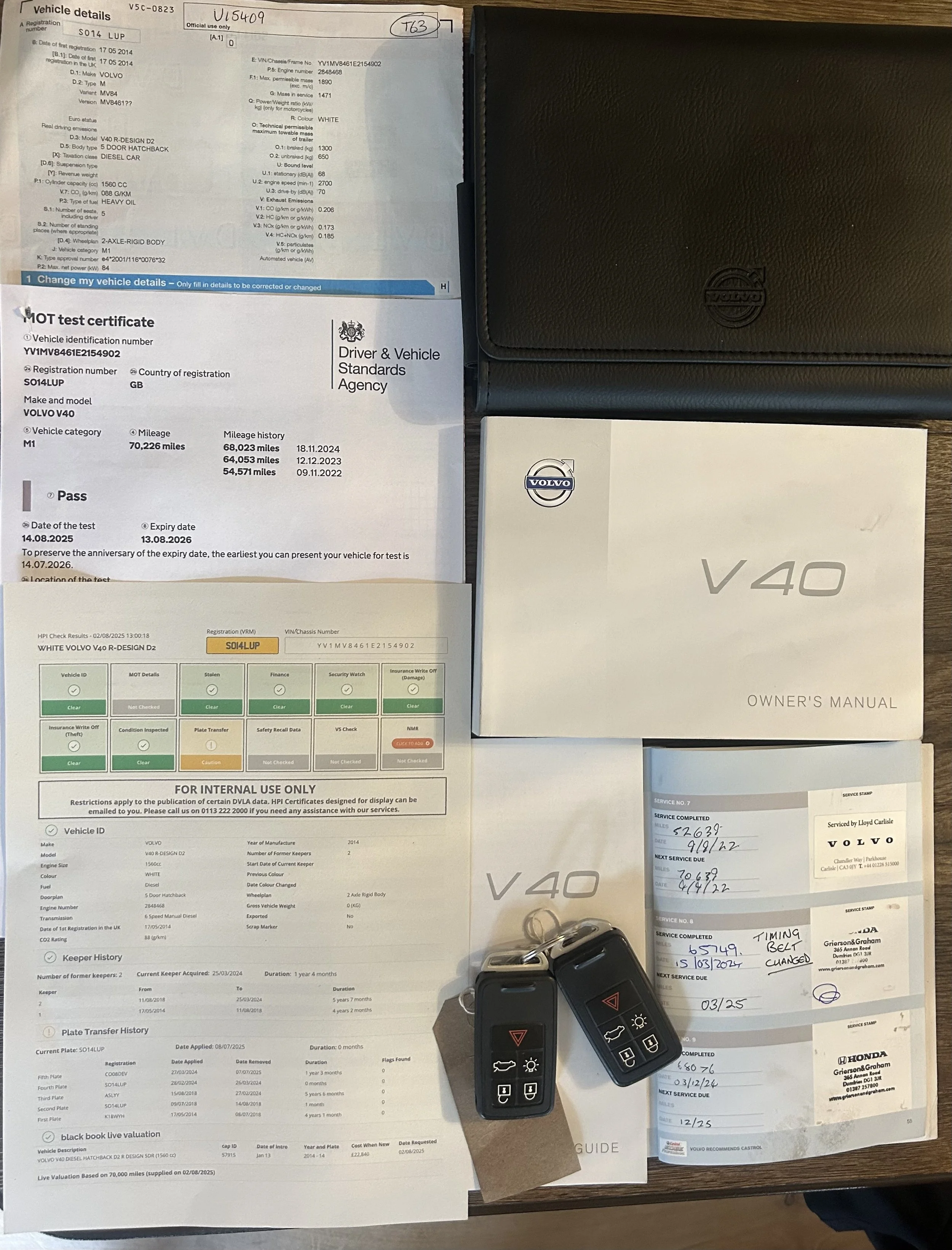 Collection of documents including a vehicle test certificate, owner's manual, service records, and key fobs for a 2014 Volvo V40.