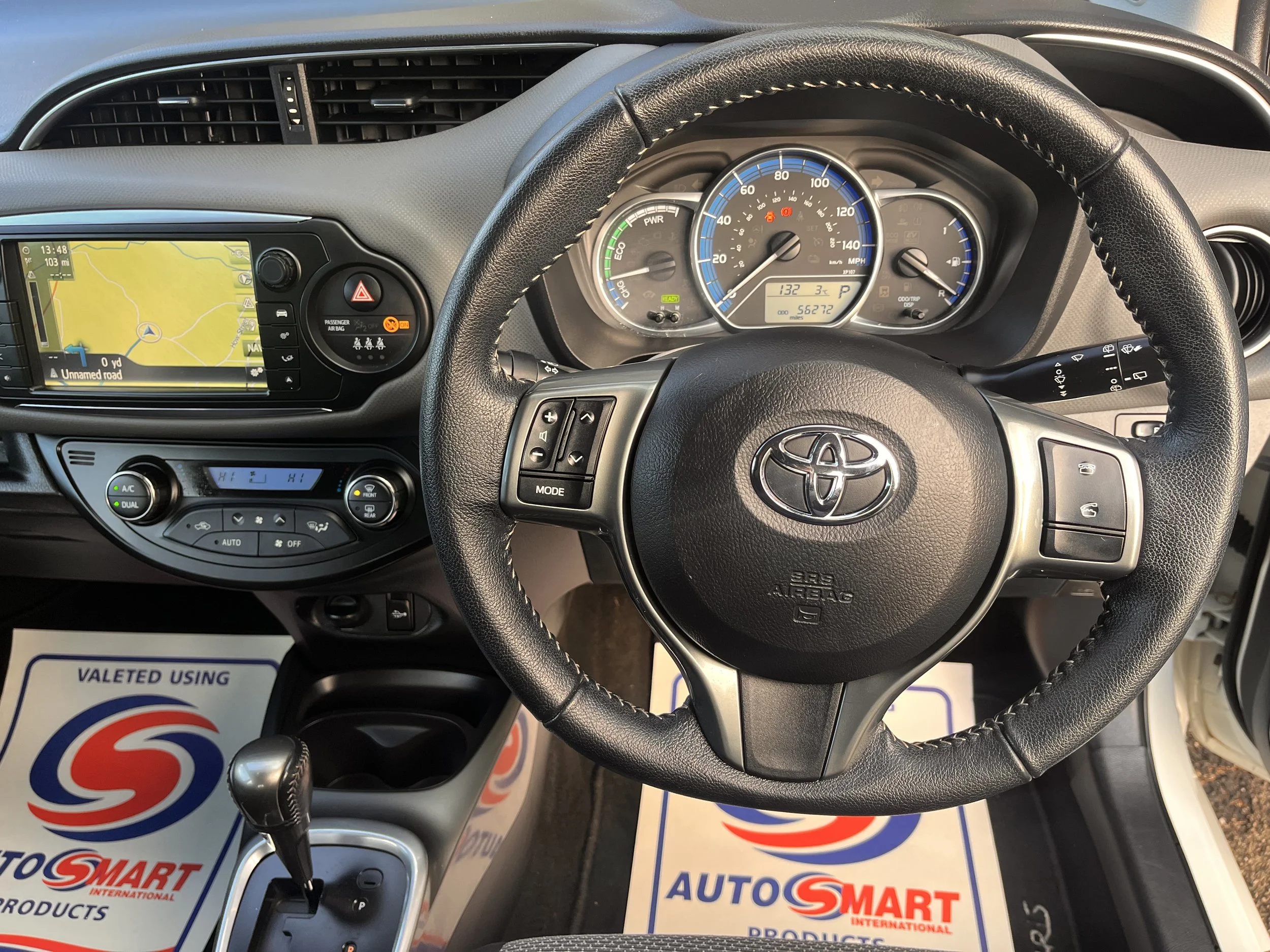 Inside view of a Toyota car dashboard showing steering wheel, speedometer, navigation screen, and climate controls.