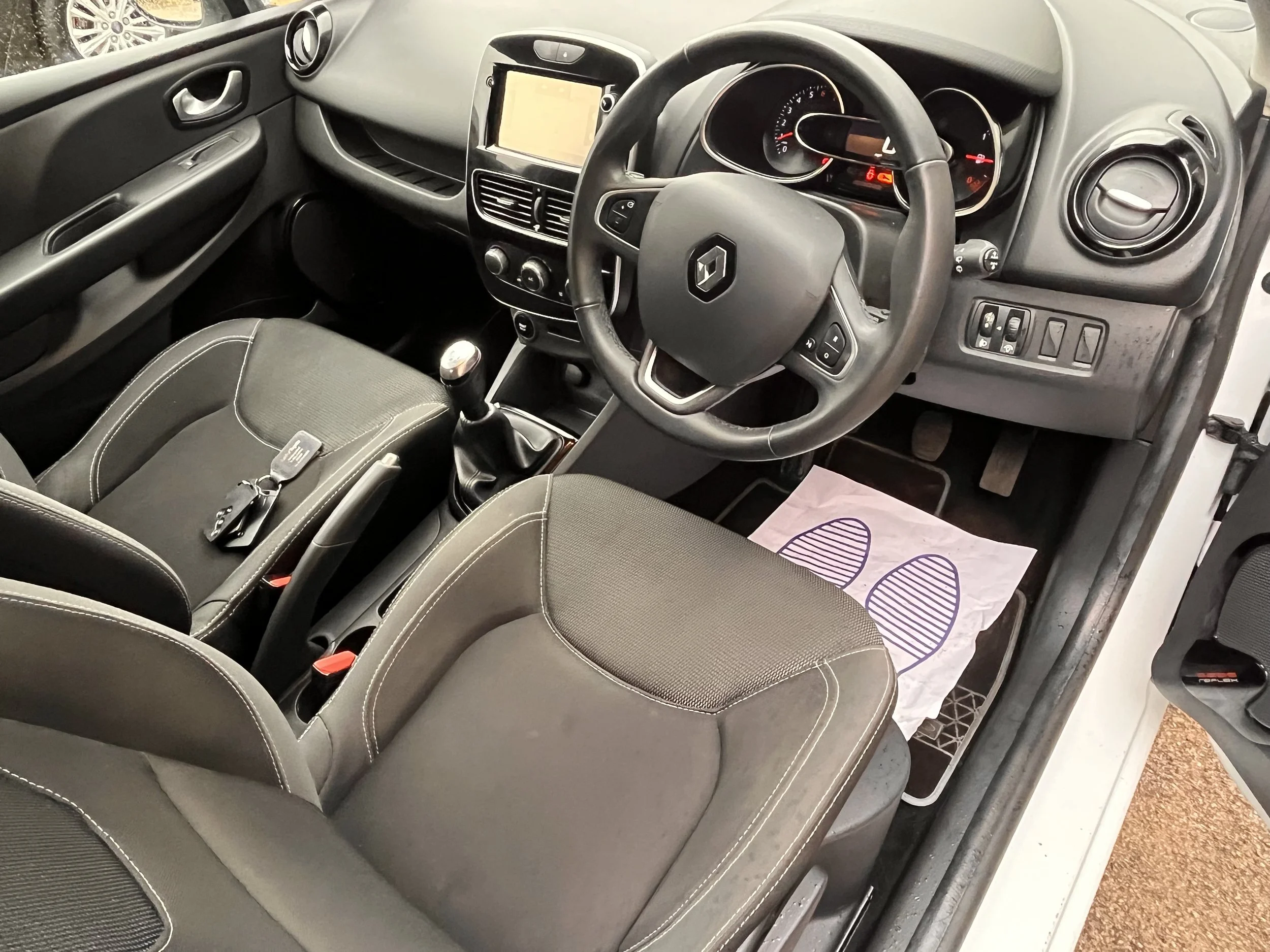 Interior of a compact car with black seats, gear shift, steering wheel, dashboard, and a road map on the passenger side floor.