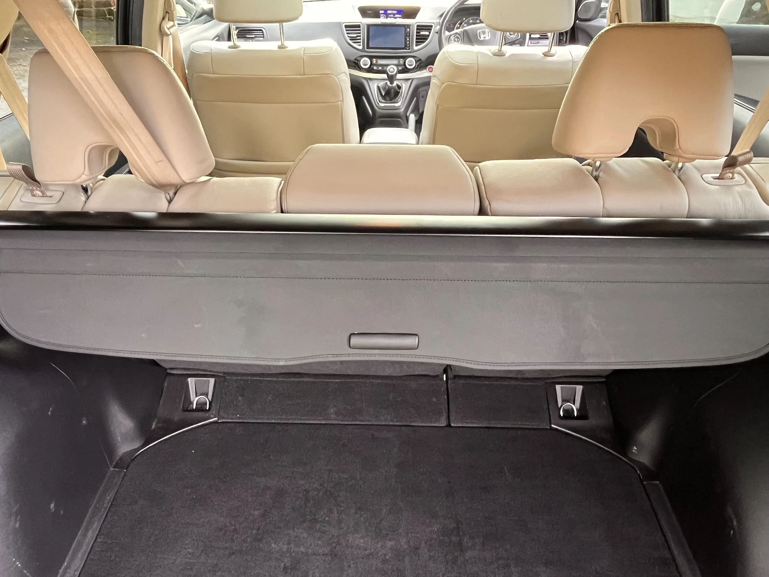 View of the interior of a car from the rear hatch, showing the beige leather back seats, headrests, and the dashboard with a touchscreen display in the front.