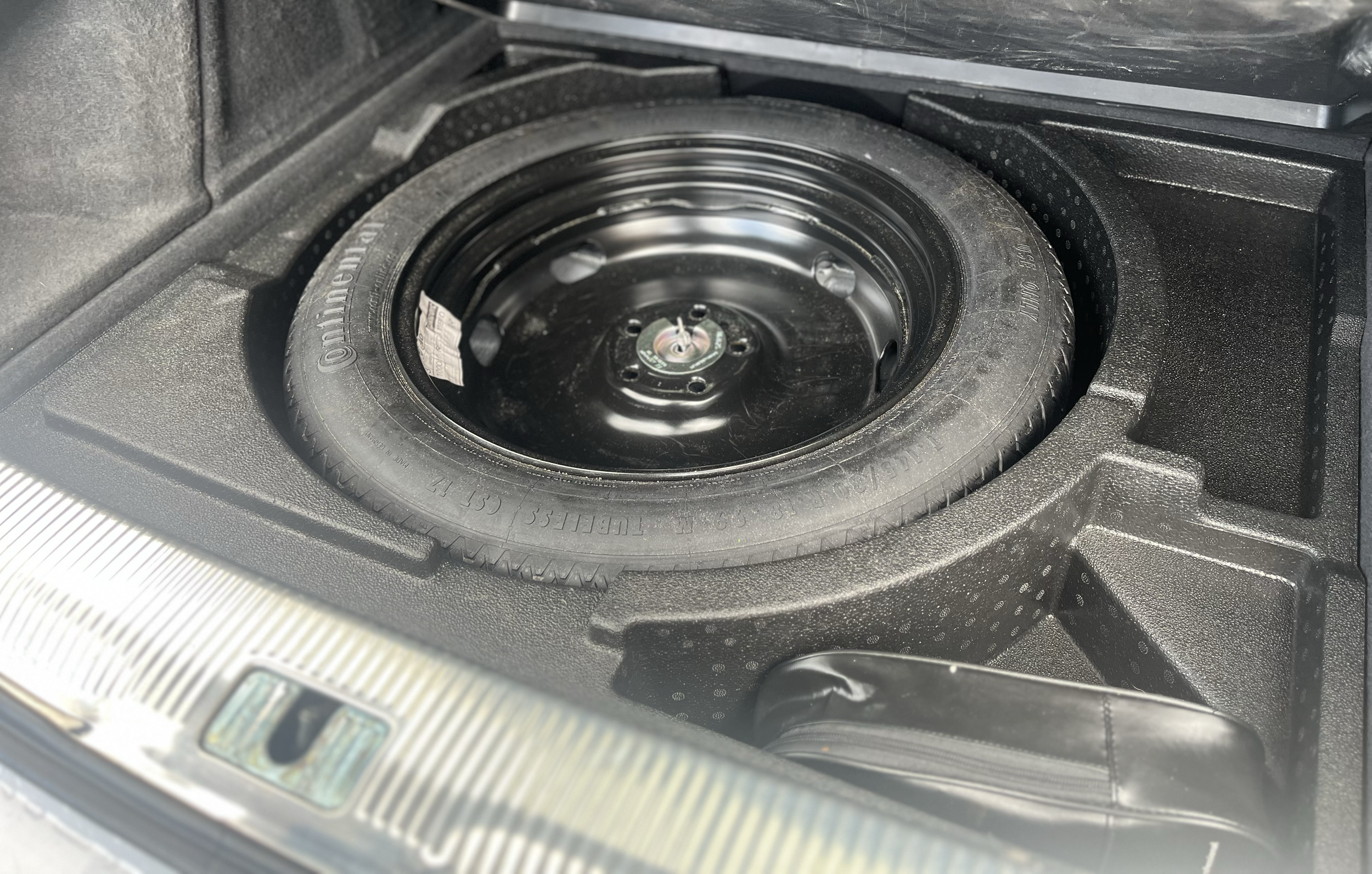 A spare tire stored in a car trunk, surrounded by black foam interior padding.