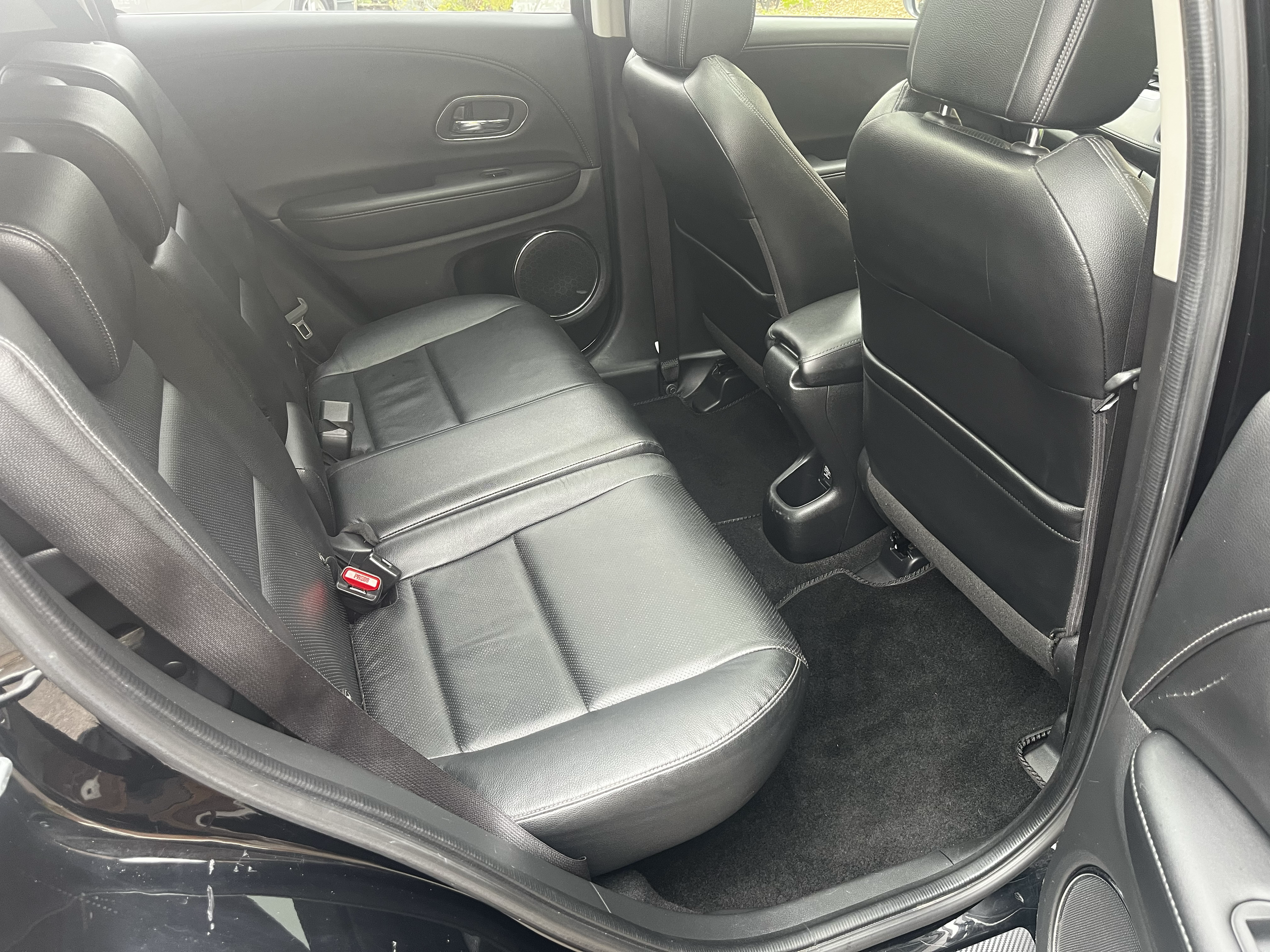 The interior of a vehicle showing the backseat with black leather seats, headrests, and the back of the front seats. The door panel and a speaker are visible on the left side.