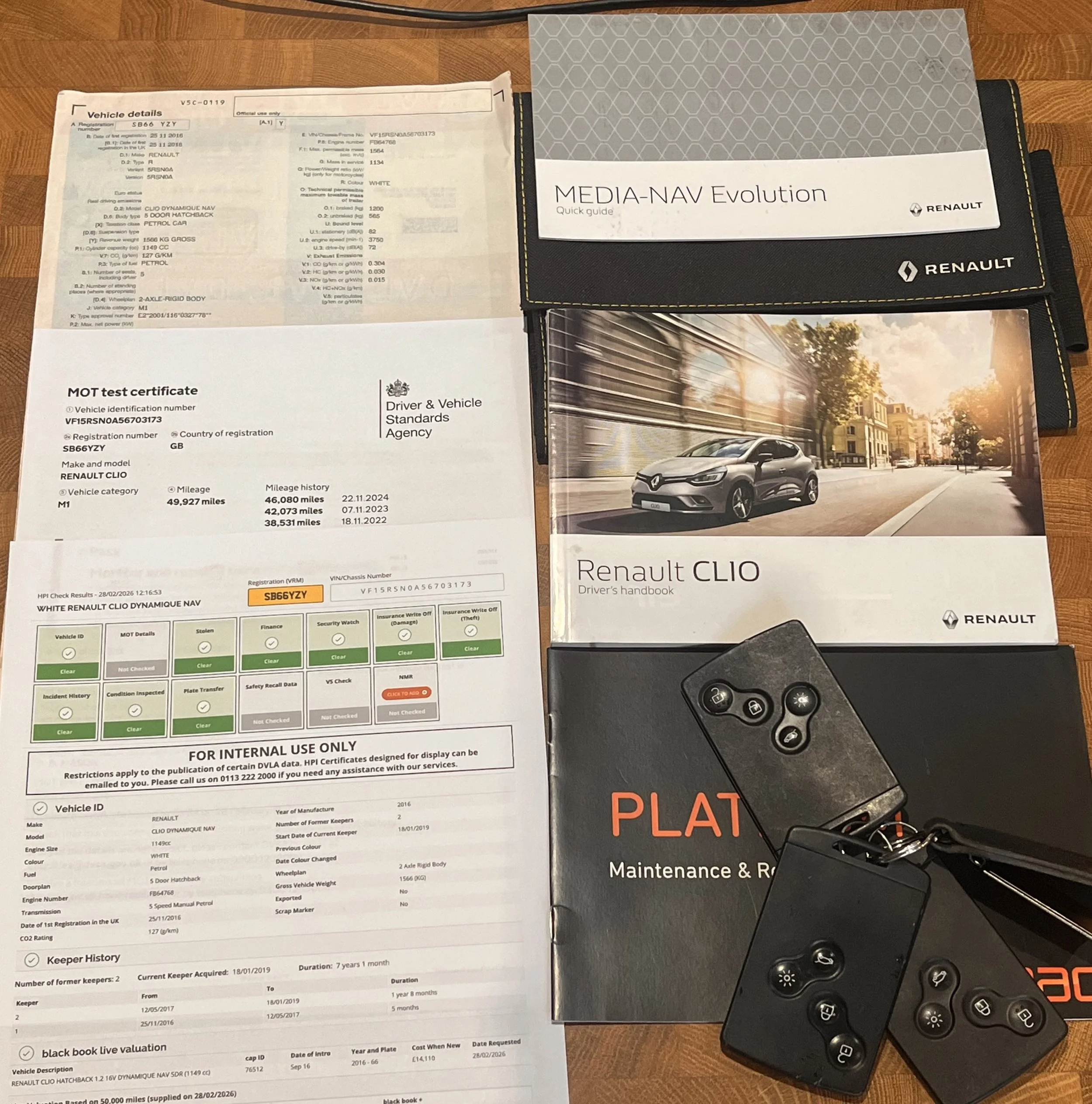 Car ownership documents, including vehicle registration, MOT test certificate, driver’s handbook, maintenance booklet, and car key fob, laid out on a wooden surface.