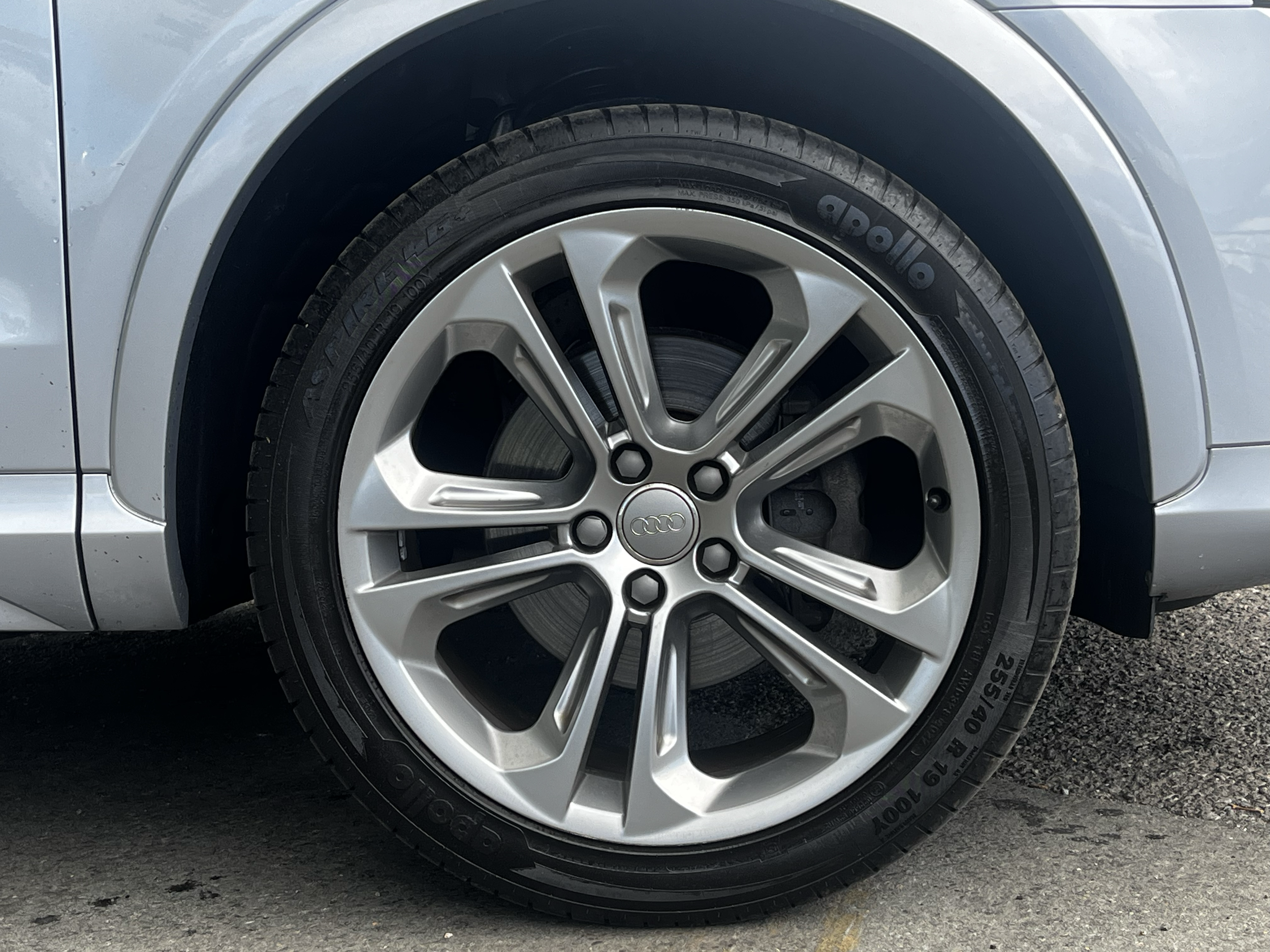 Close-up view of a silver car wheel with black tire, showing the car's body and part of the wheel well.