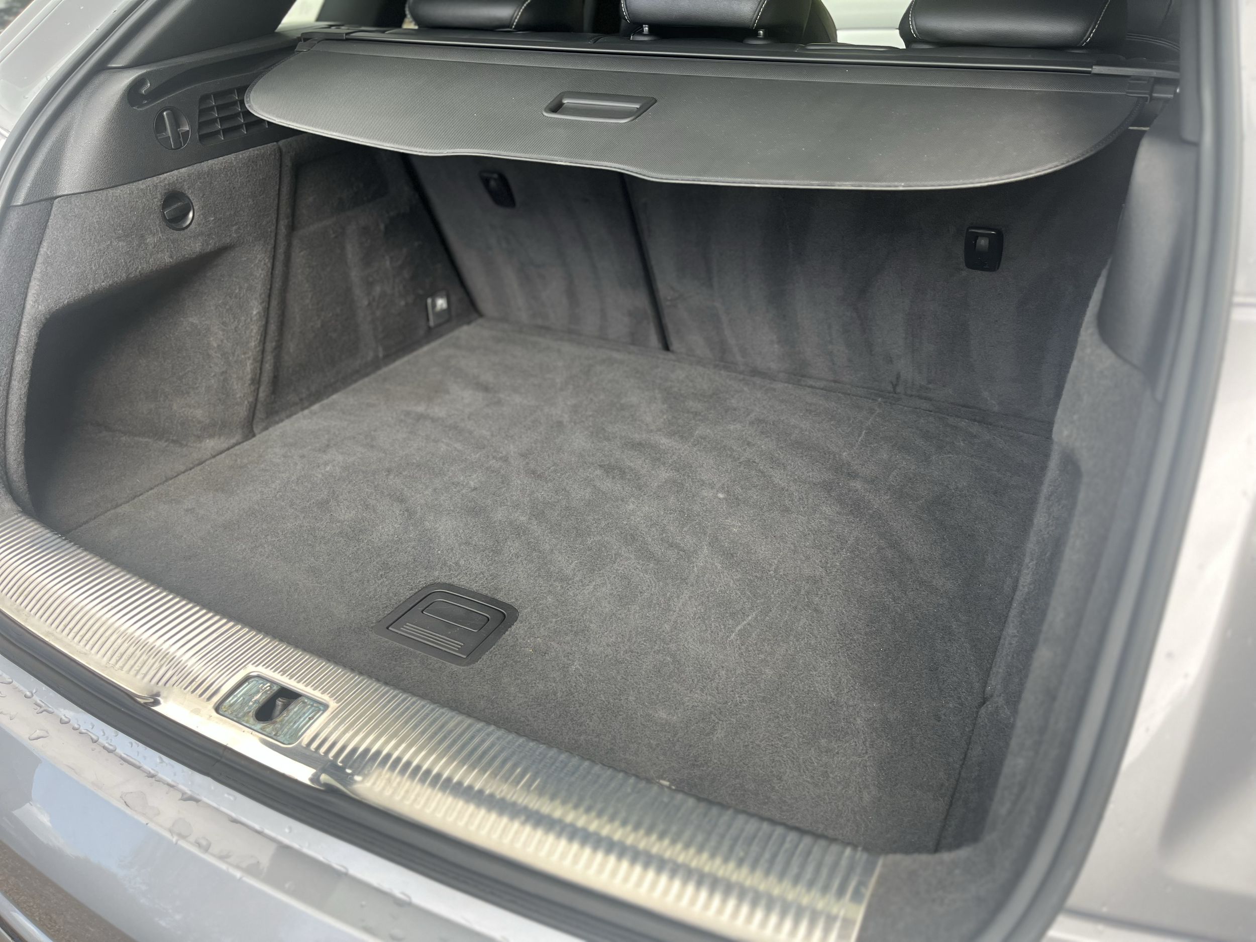 The trunk of a car with a retractable cover, carpeted interior, and a metal latch at the edge of the trunk opening.