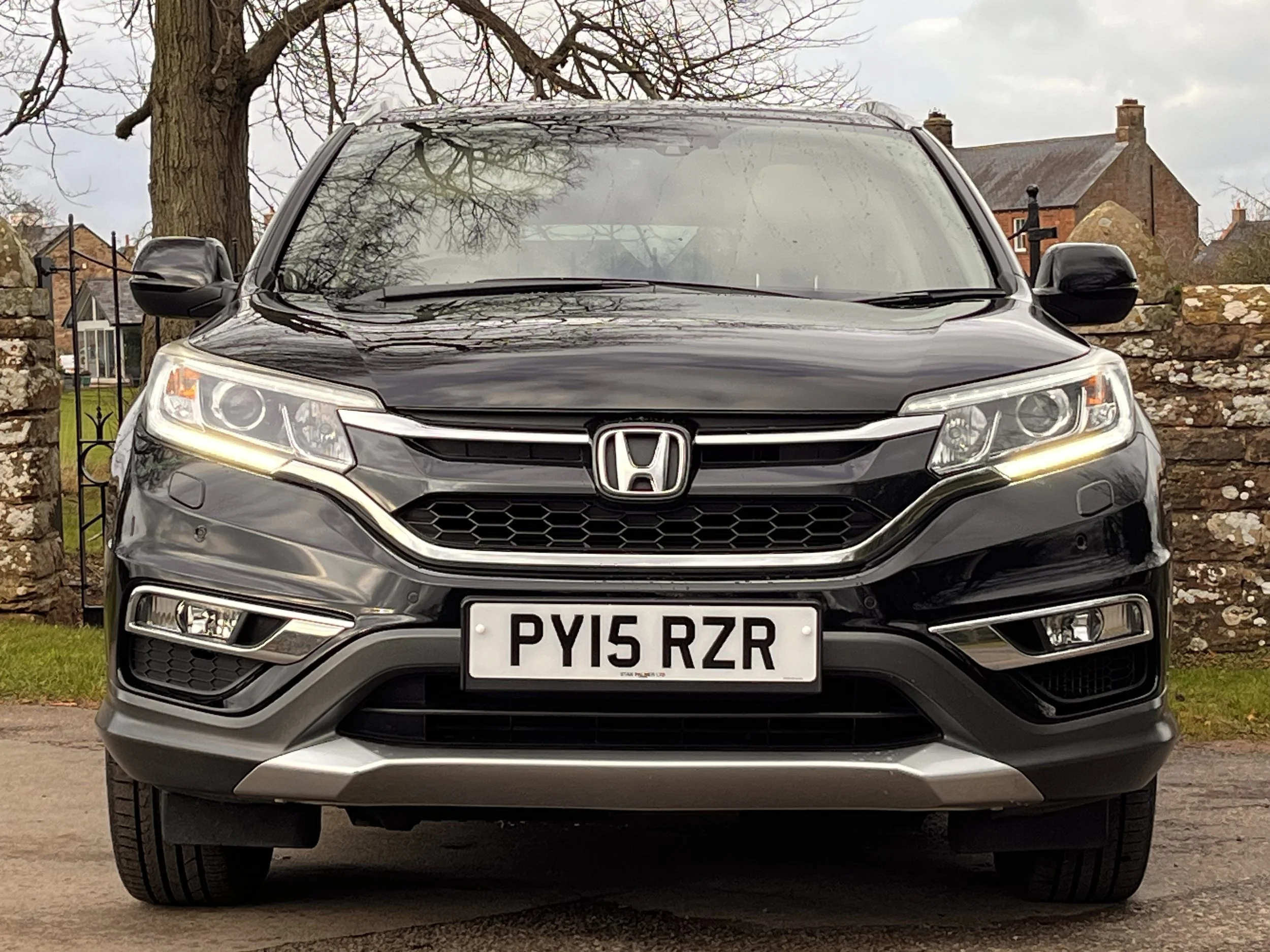 Front view of a black Honda CR-V parked outdoors with a stone wall and trees in the background.