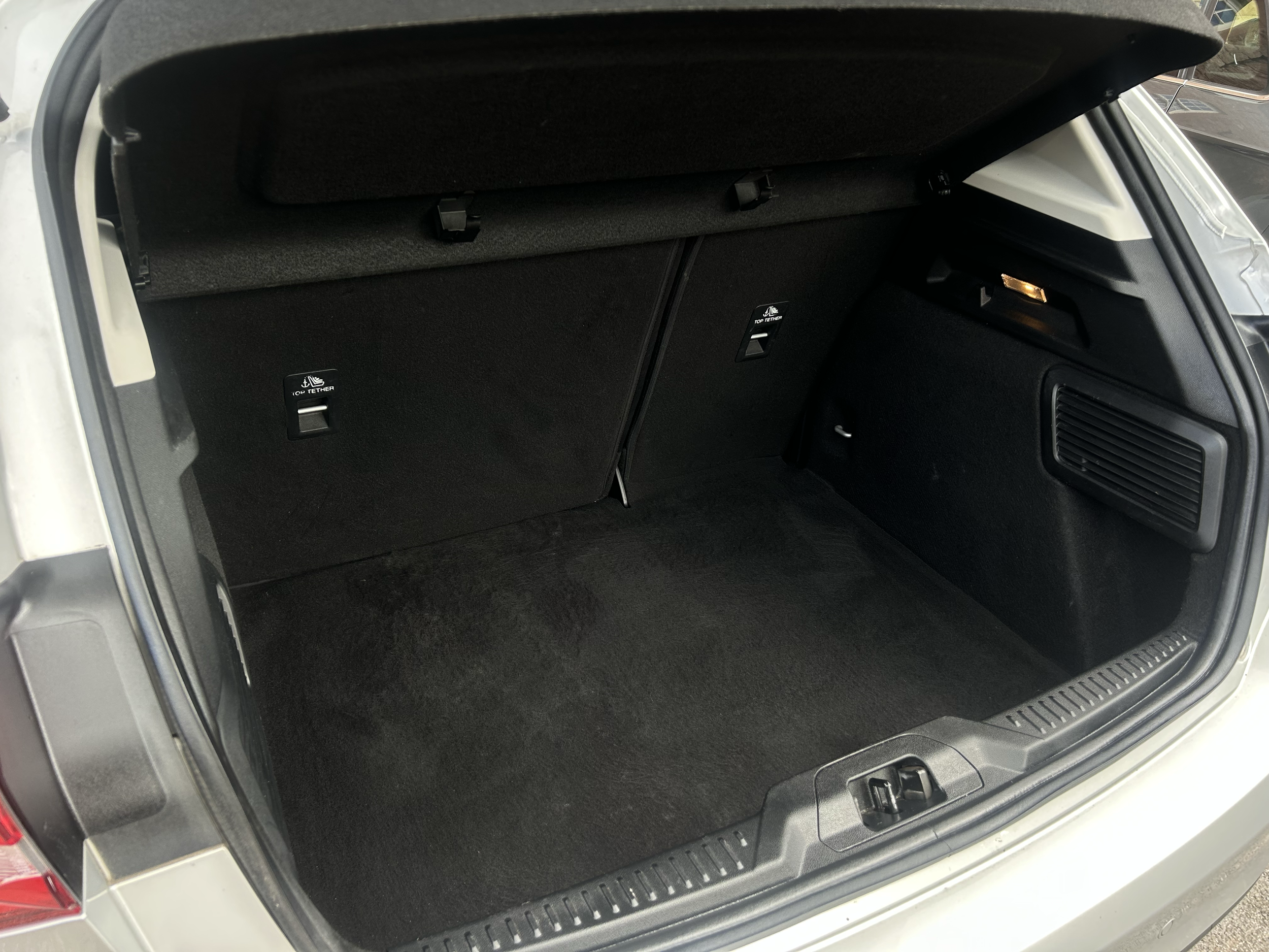 Open car trunk showing empty storage space with black carpeting and a small compartment on the right side.