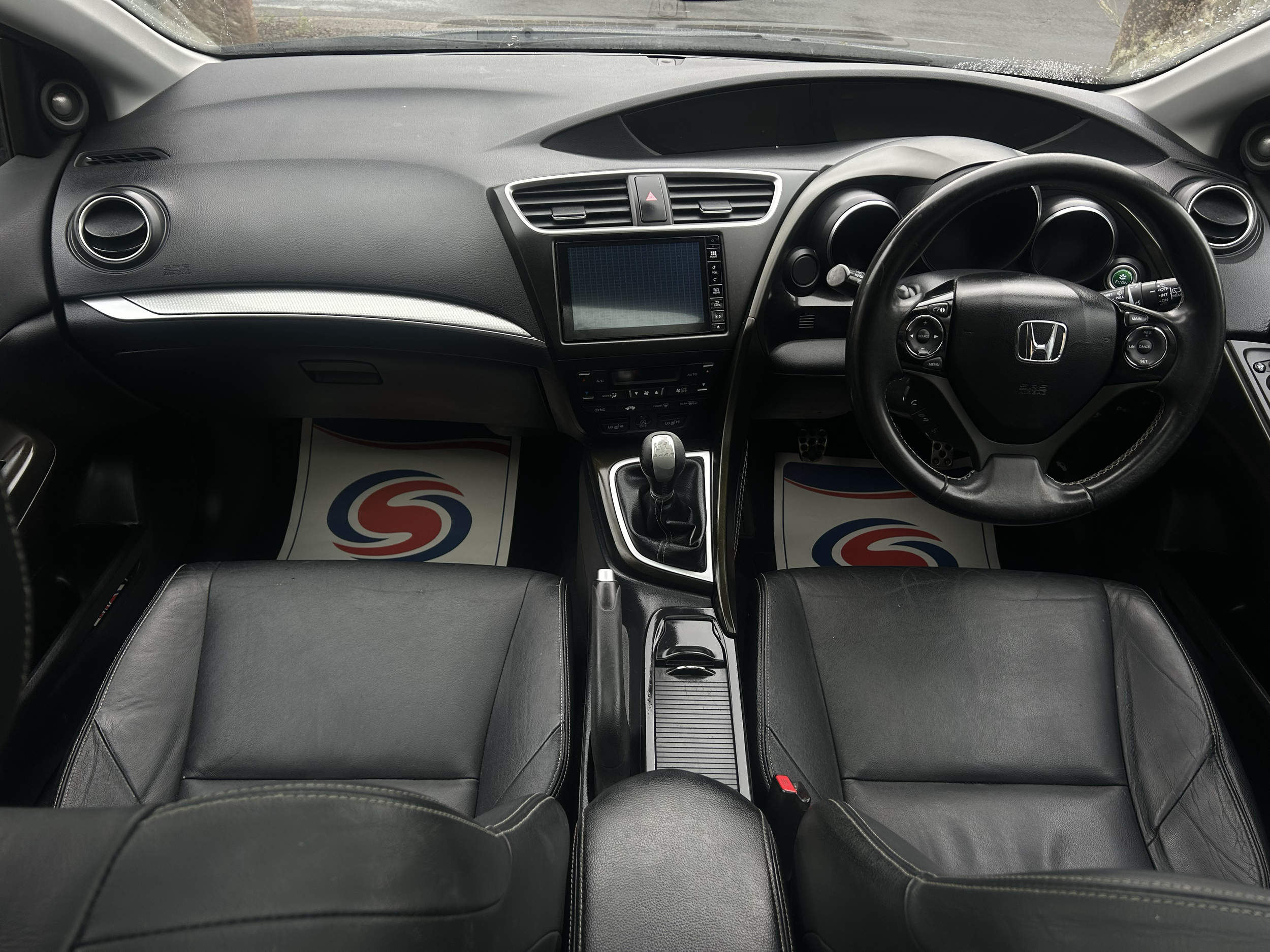 Photo of the interior of a car, including the dashboard, steering wheel, and front seats, with a view through the windshield showing the road ahead.