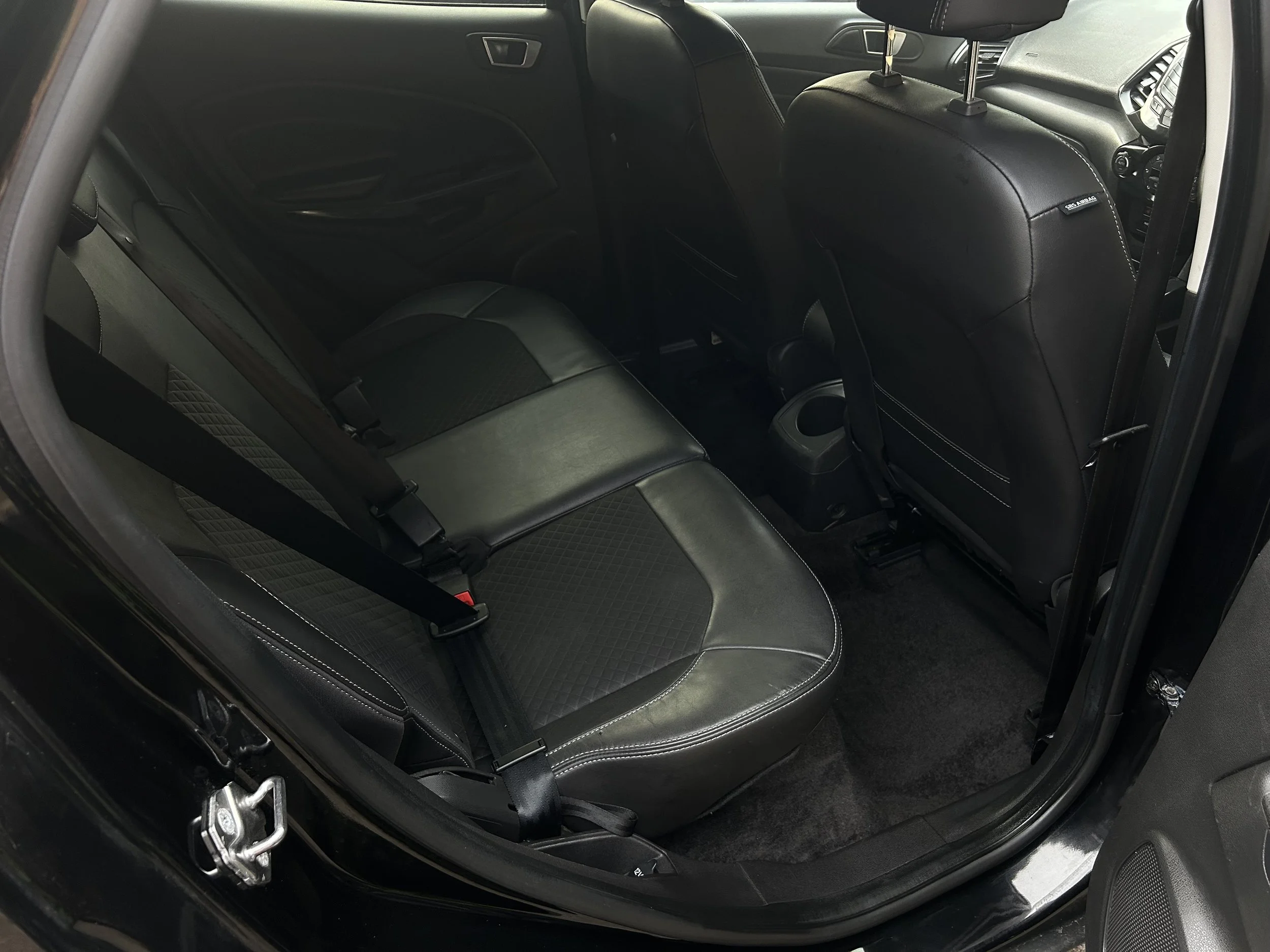 Interior of a car showing the backseat with black leather seats and seat belts, and the front seats with headrests.