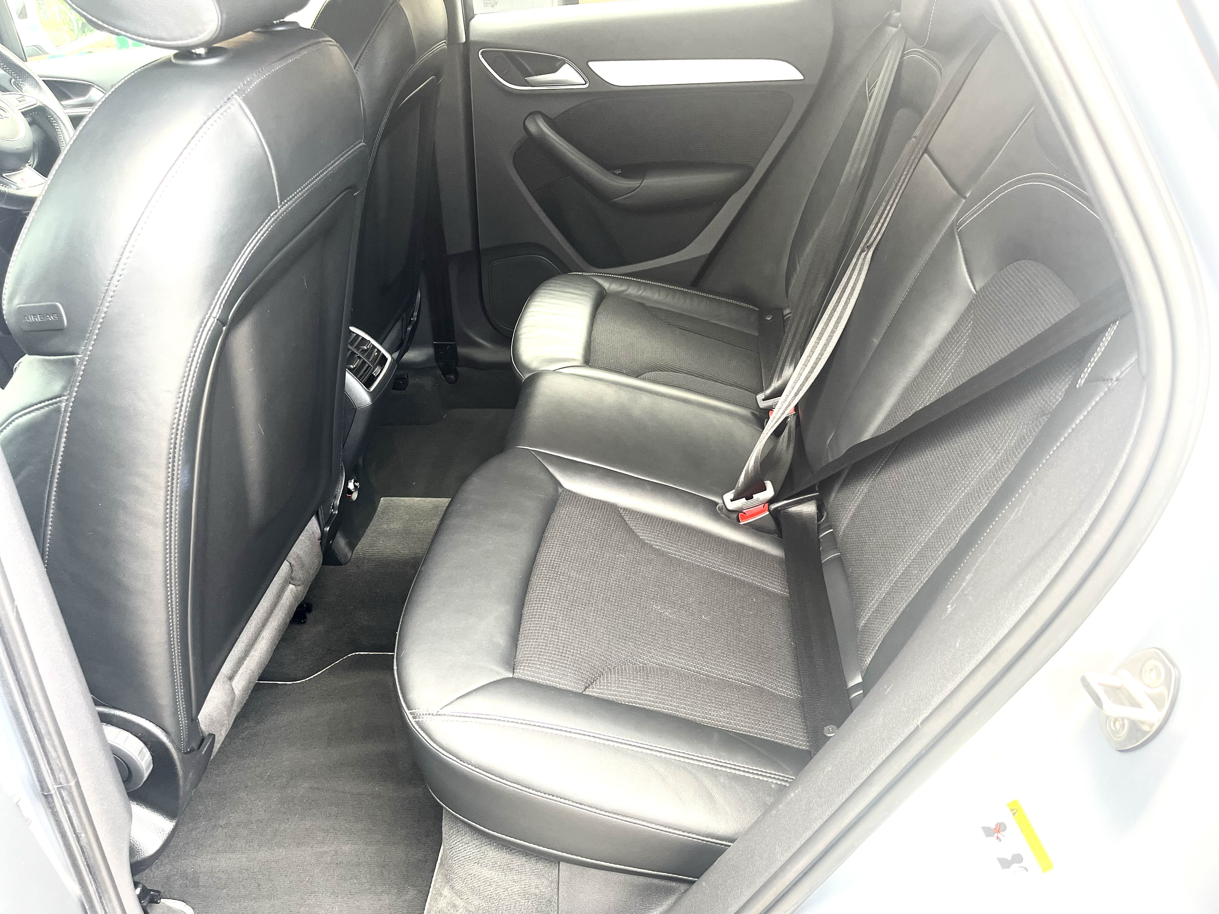 The backseat interior of a modern car with black leather seats and a gray carpeted floor.
