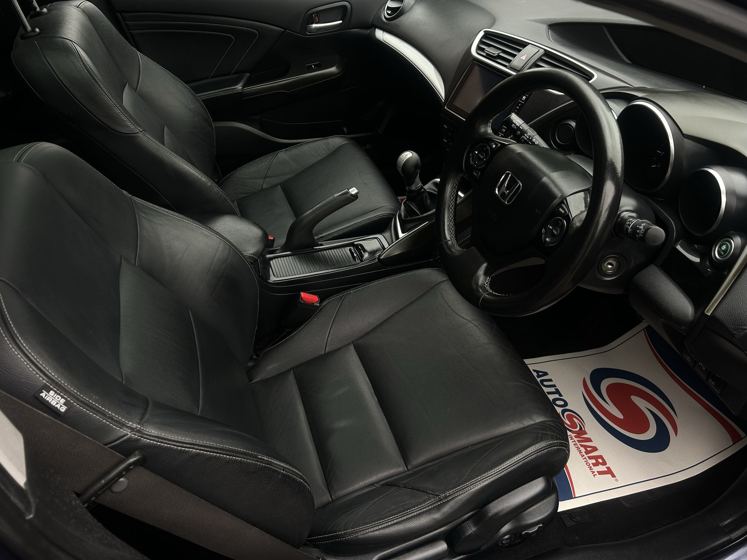 The interior of a black Honda car with black leather seats, a gear shift, steering wheel, dashboard, and an infotainment screen.