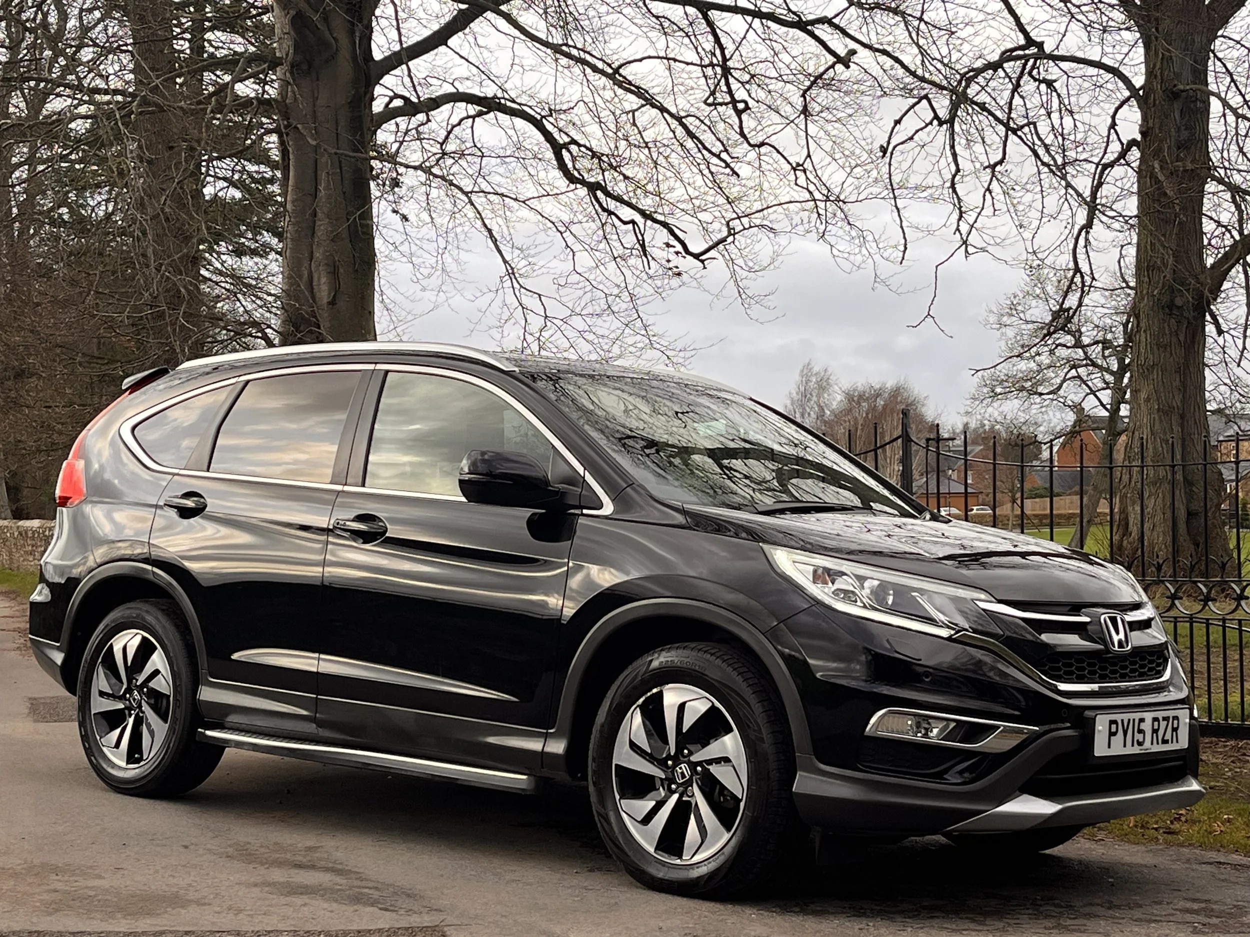 Black Honda SUV parked outdoors near trees and a fence on a cloudy day.