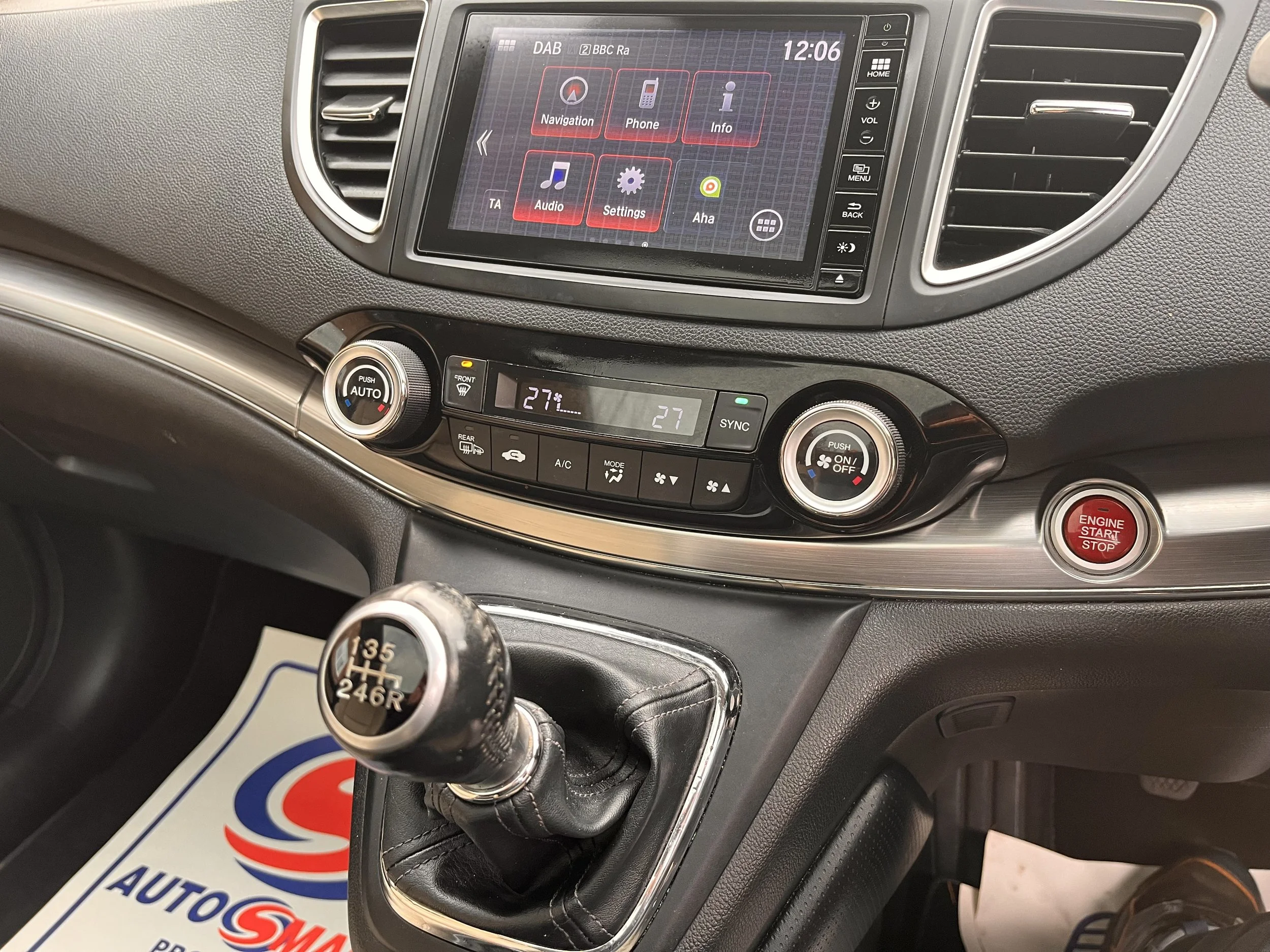 Inside view of a car dashboard showing a touchscreen navigation system, climate controls, a gear shift, and an engine start/stop button.