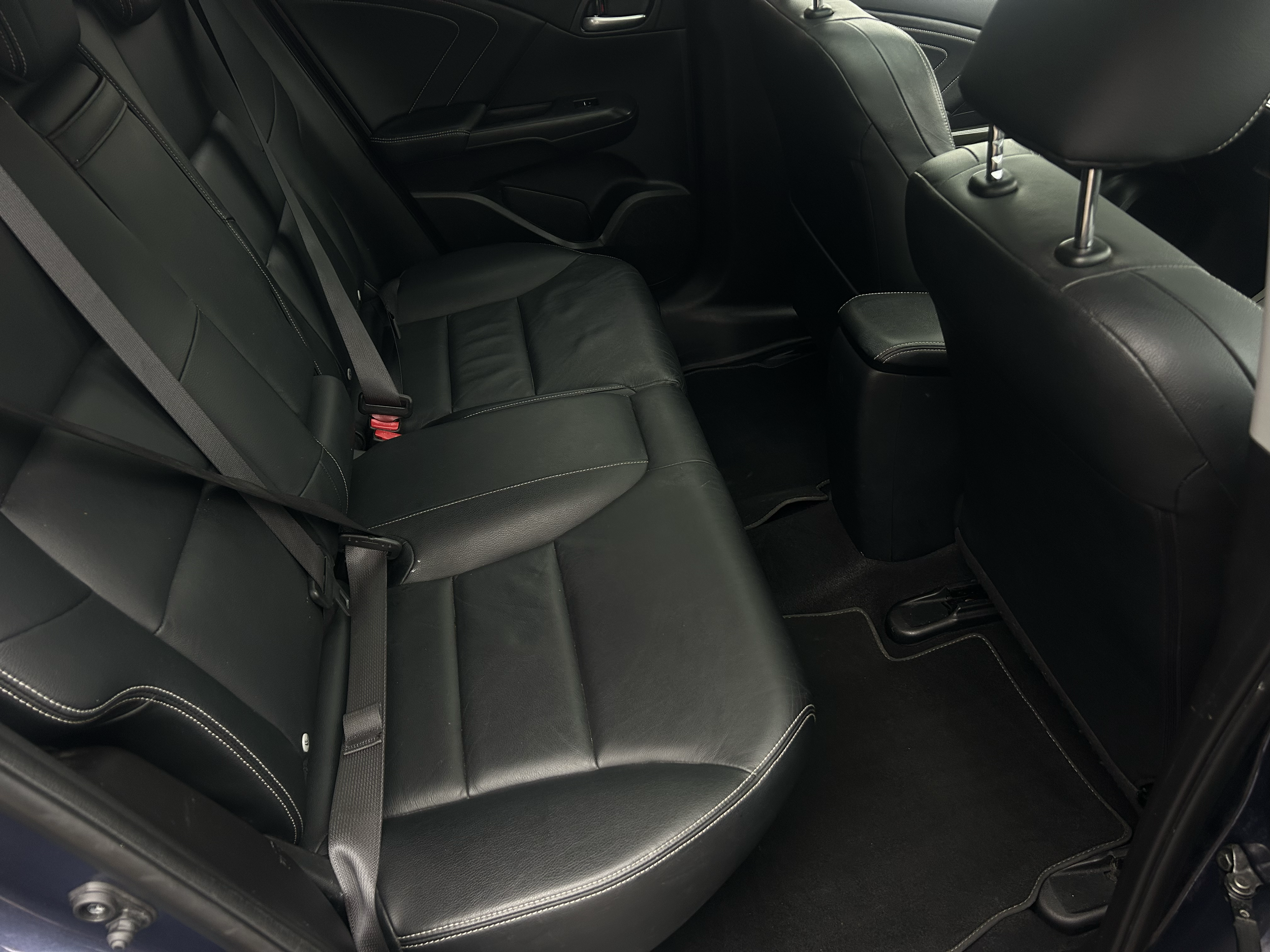 The image shows the back seat of a black car with leather upholstery, headrests, and seat belts.