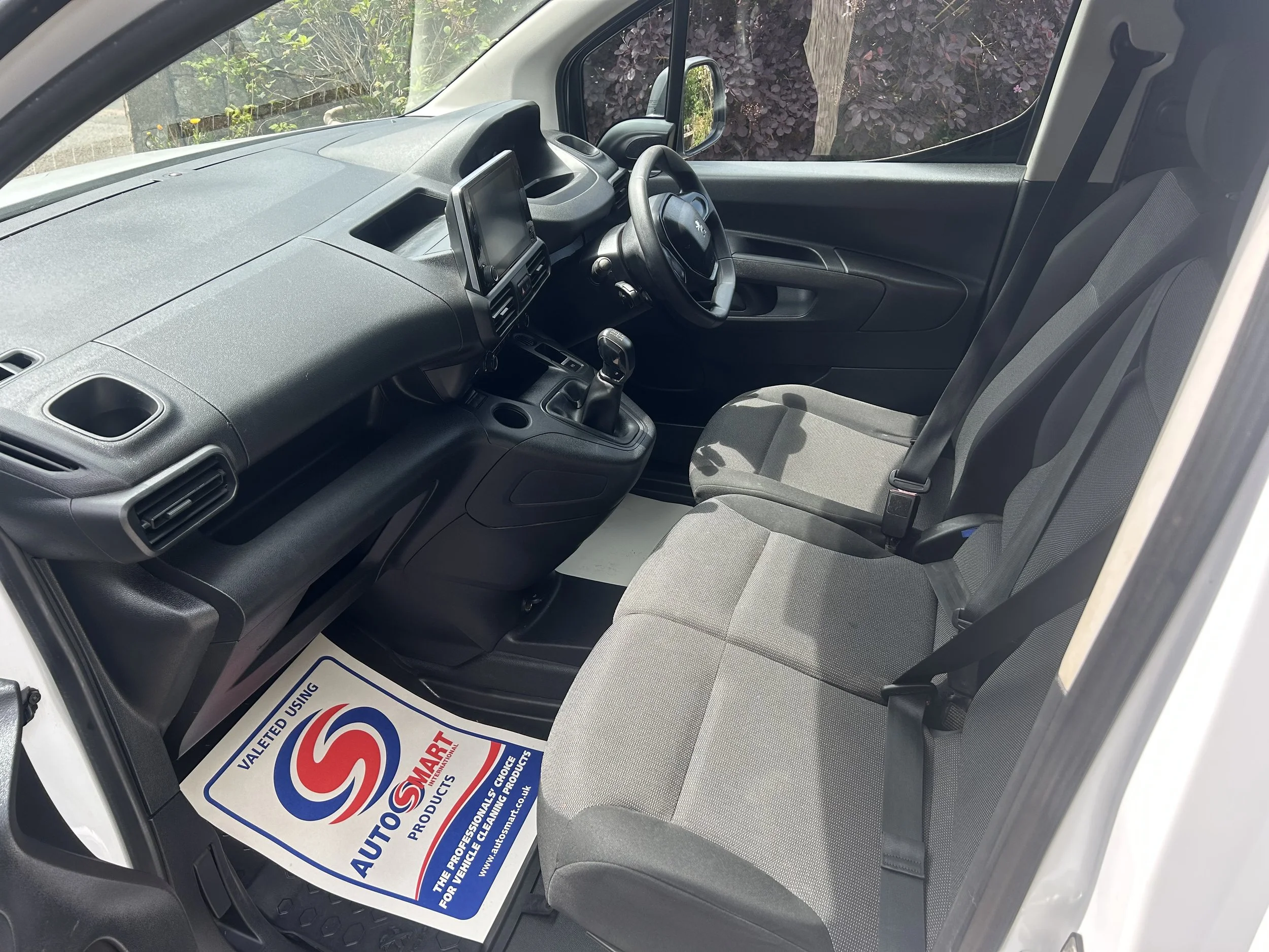 Interior of a vehicle showing the front seats, dashboard, steering wheel, gear shift, and a floor mat with an AutoSmart logo.