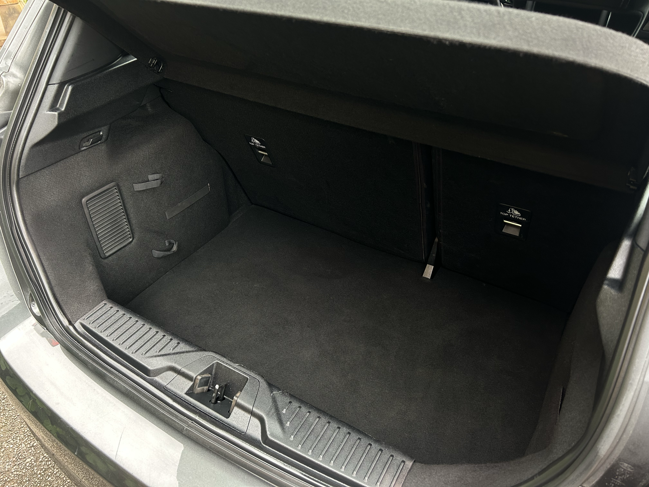 Open car trunk showing clean, black interior with a flat floor and small storage compartments on each side.