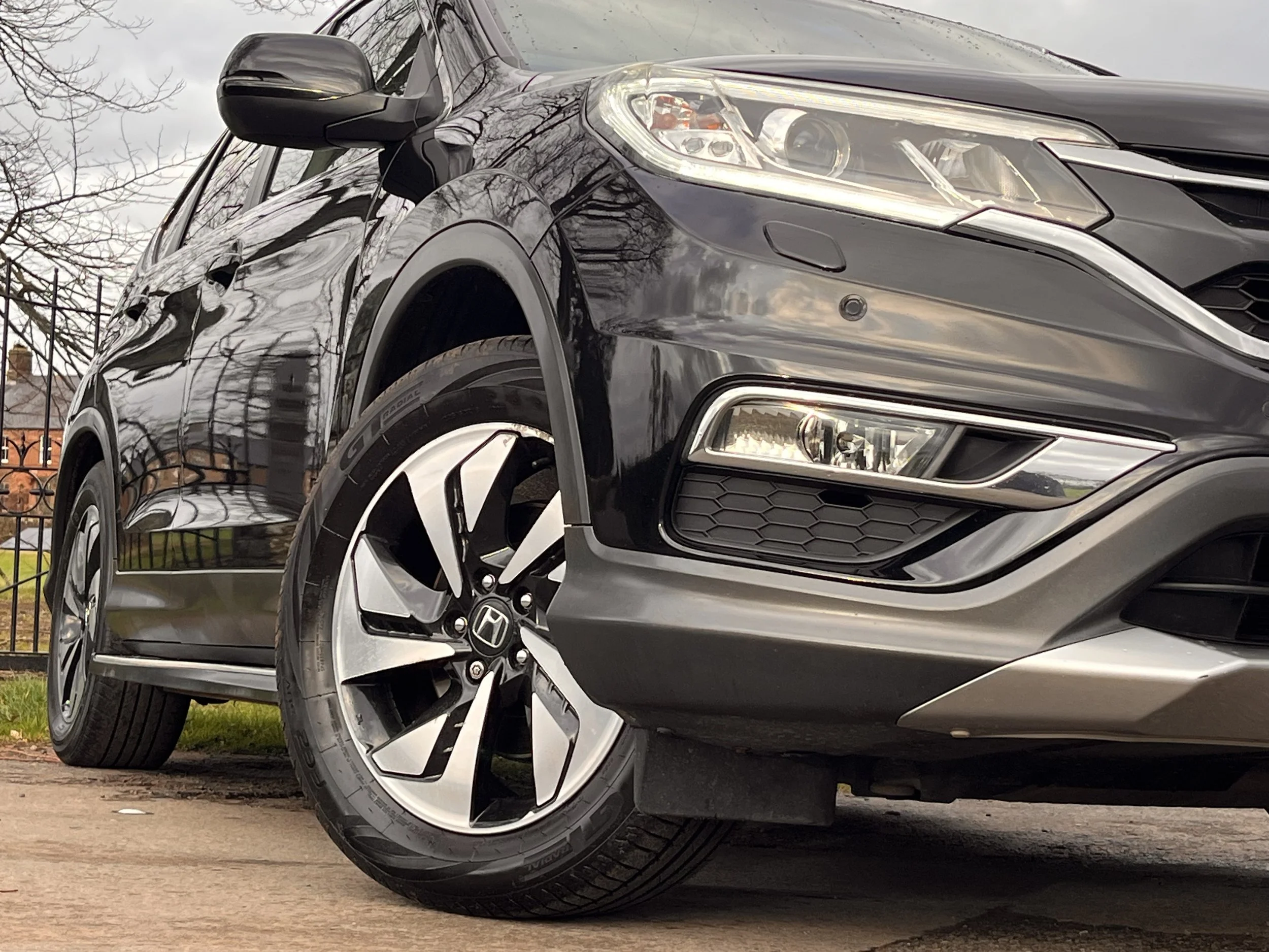 Close-up of the front side of a black Honda SUV parked on a driveway with a house and trees in the background.