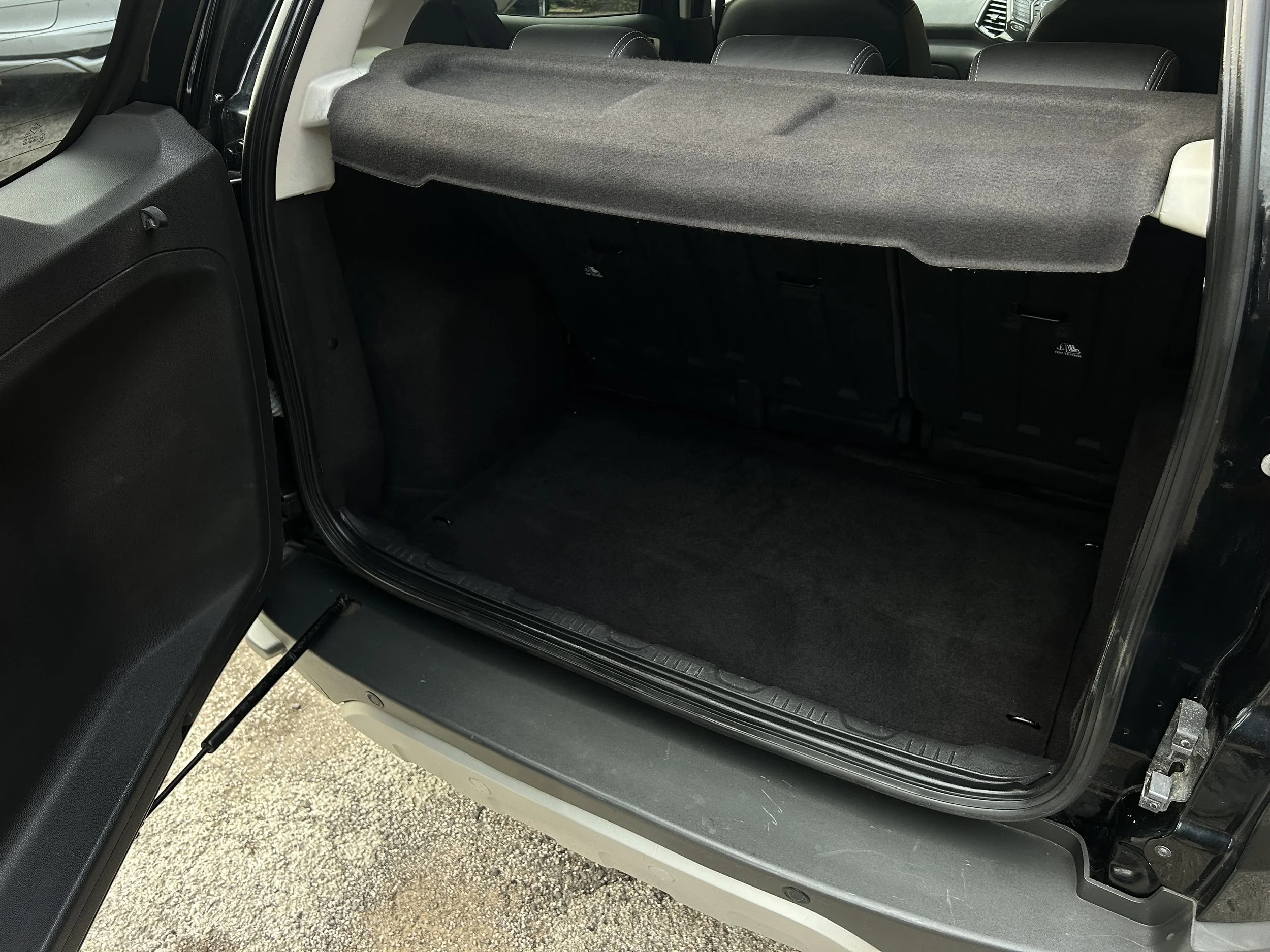The rear cargo area of a black SUV, with the back door open, showing a clean space with folded rear seats and a cargo cover in place.