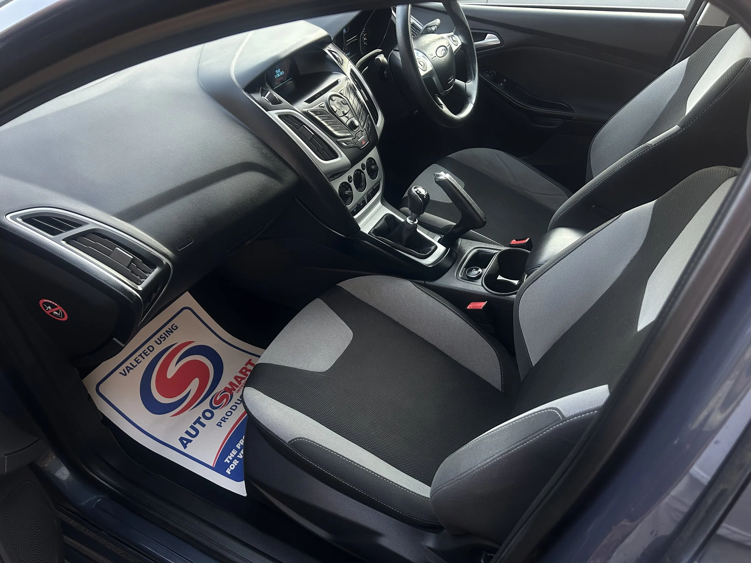 Interior view of a car showing the driver's seat, front passenger seat, dashboard, steering wheel, gear shift, and center console.